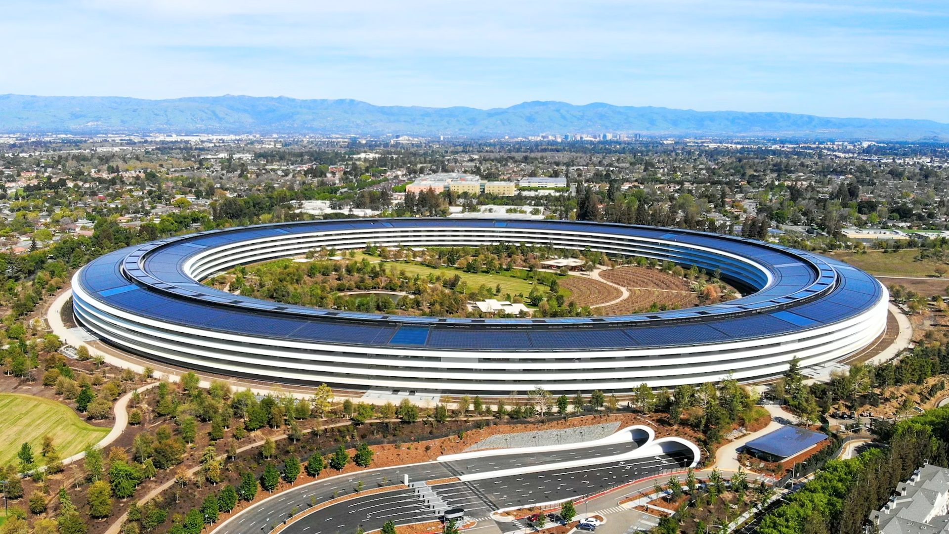 An aerial view of the ring-shaped Apple Park building surrounded by landscaped grounds.