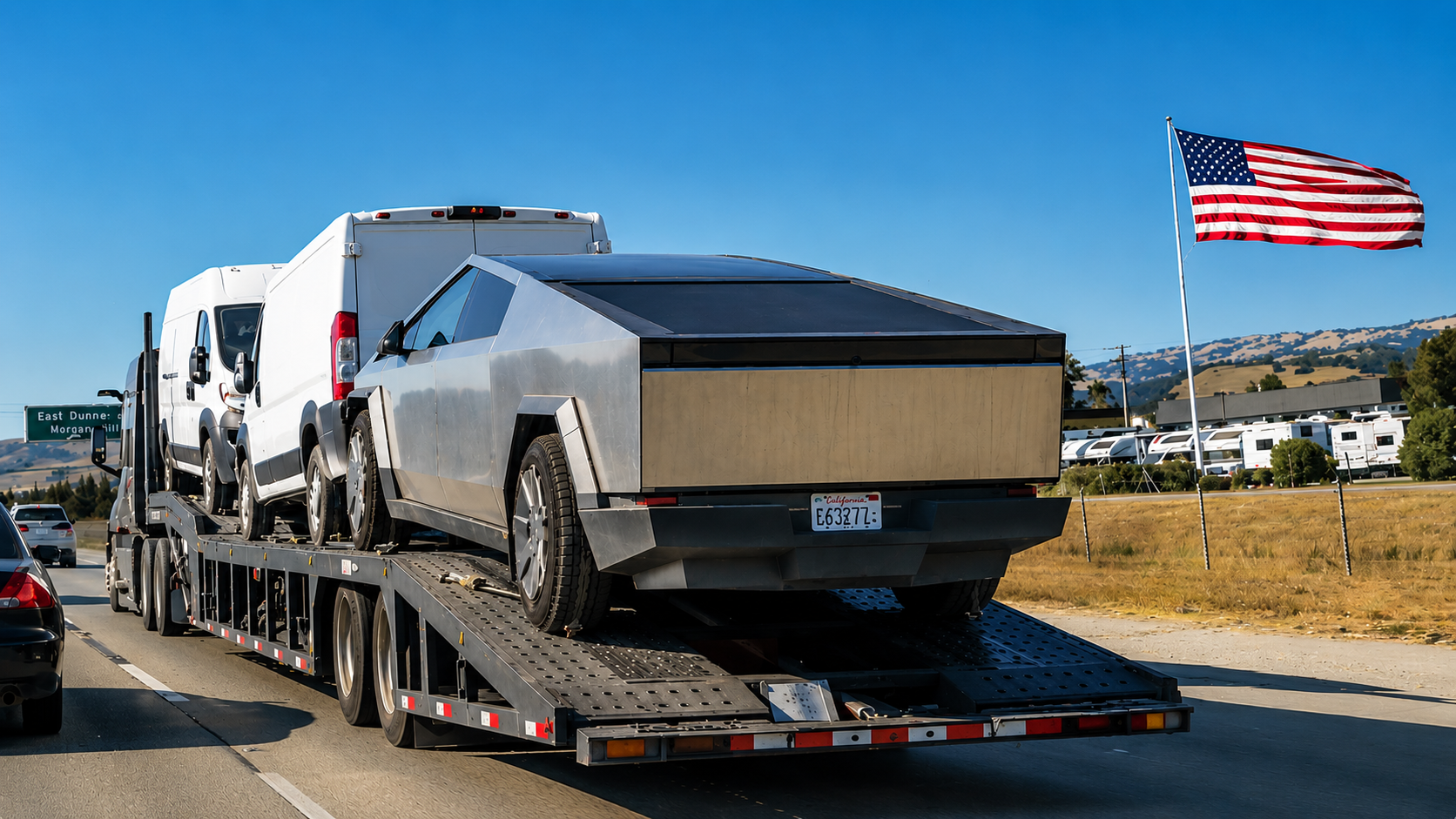 A Tesla Cybertruck and white transport vans loaded onto a flatbed car hauler driving on a highway.