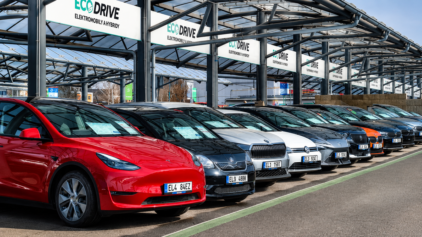 A red Tesla Model Y parked in a row of electric and hybrid cars under an EcoDrive dealership canopy.