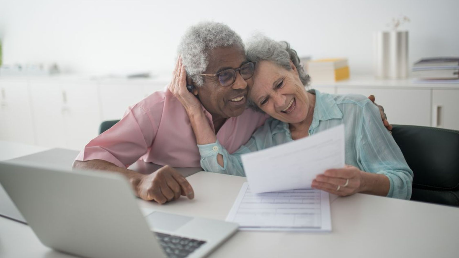 Older couple smiling while reviewing paperwork together at home.