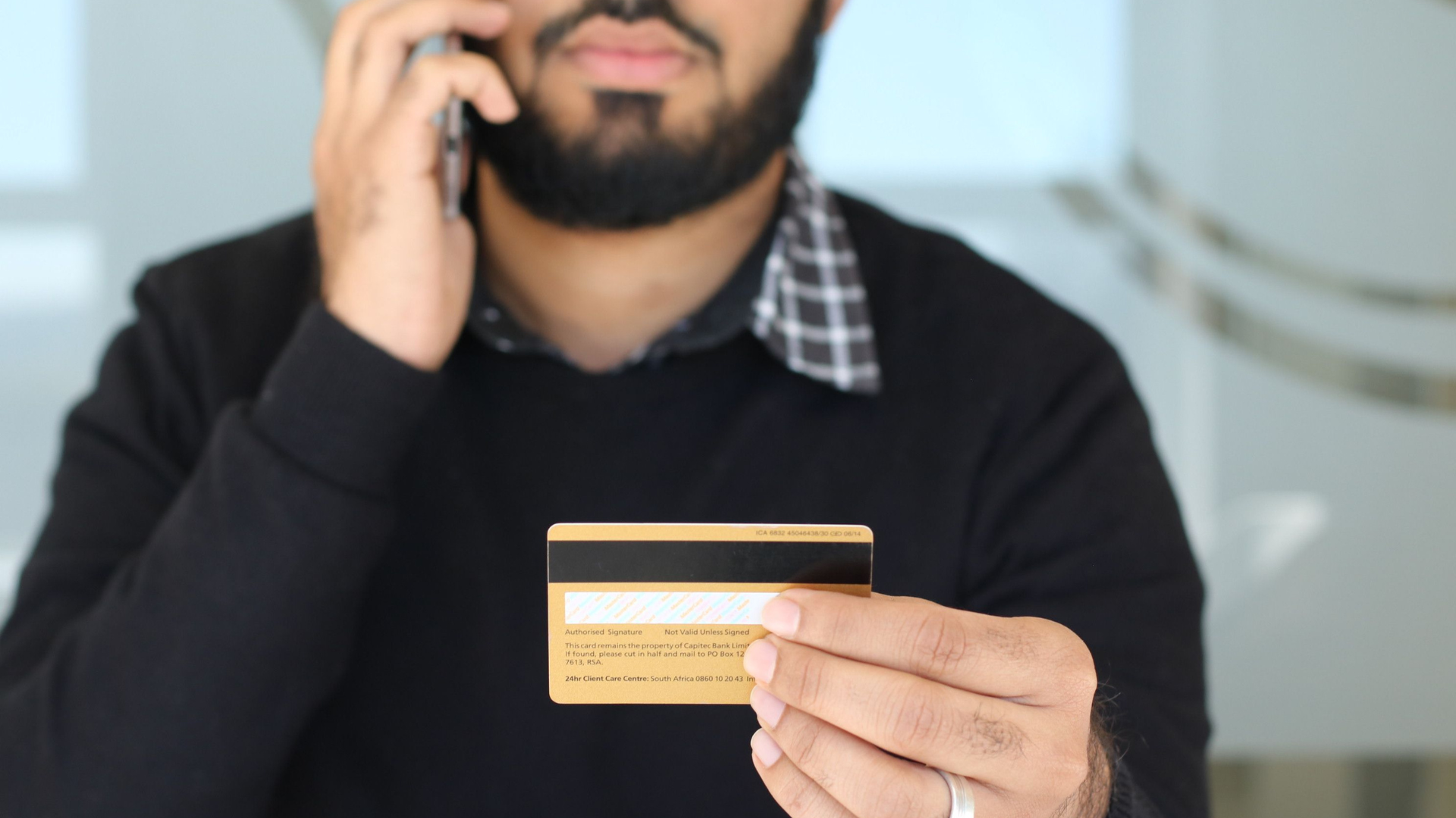  A close-up focus on a man holding up the back of a Capitec Bank credit card while talking on his mobile phone.