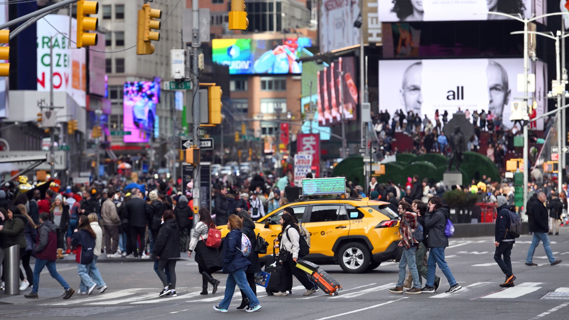 Crowds of people crossing a busy New York City street intersection.