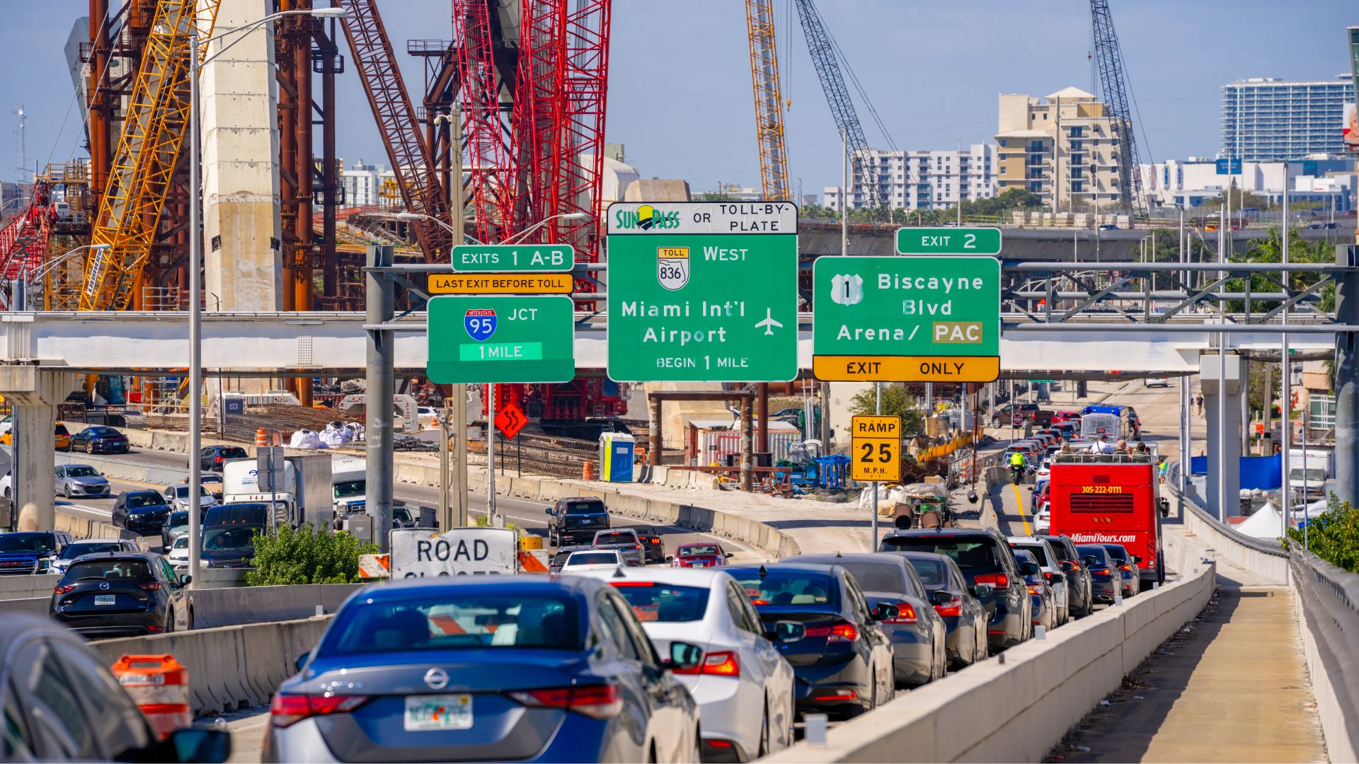 Miami highway traffic backed up near construction cranes and overhead road signs.
