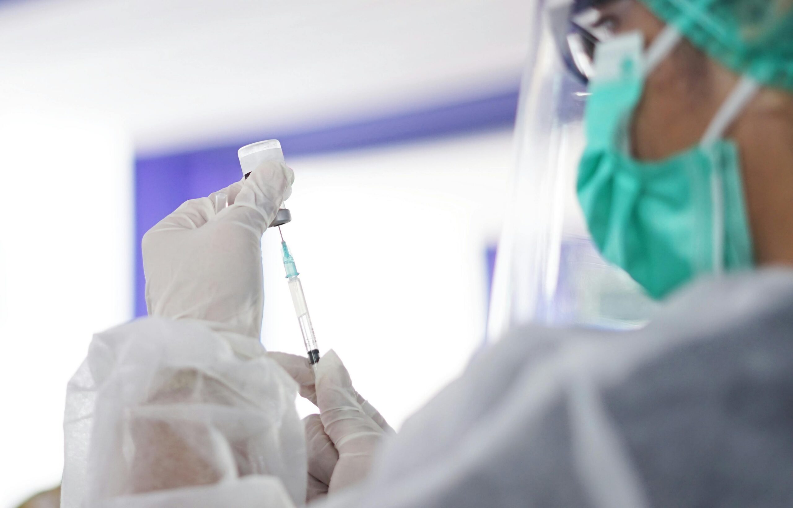 Healthcare worker wearing protective equipment prepares a vaccine dose from a vial.