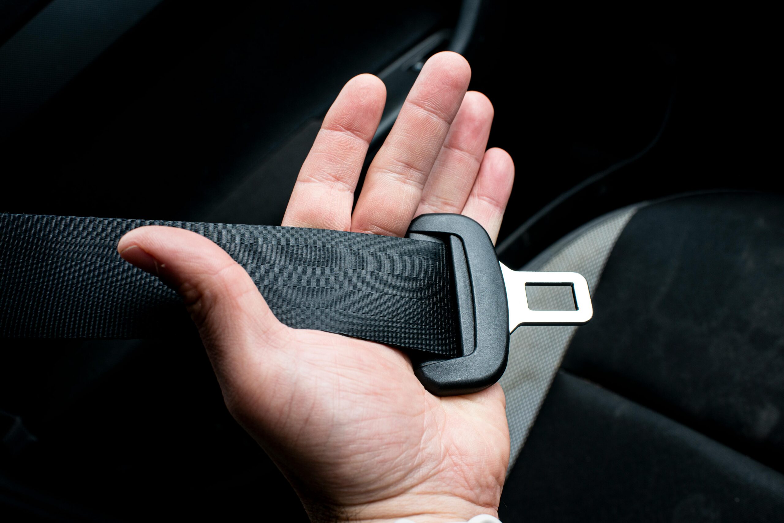Hand holding a vehicle seat belt before fastening it inside a car.