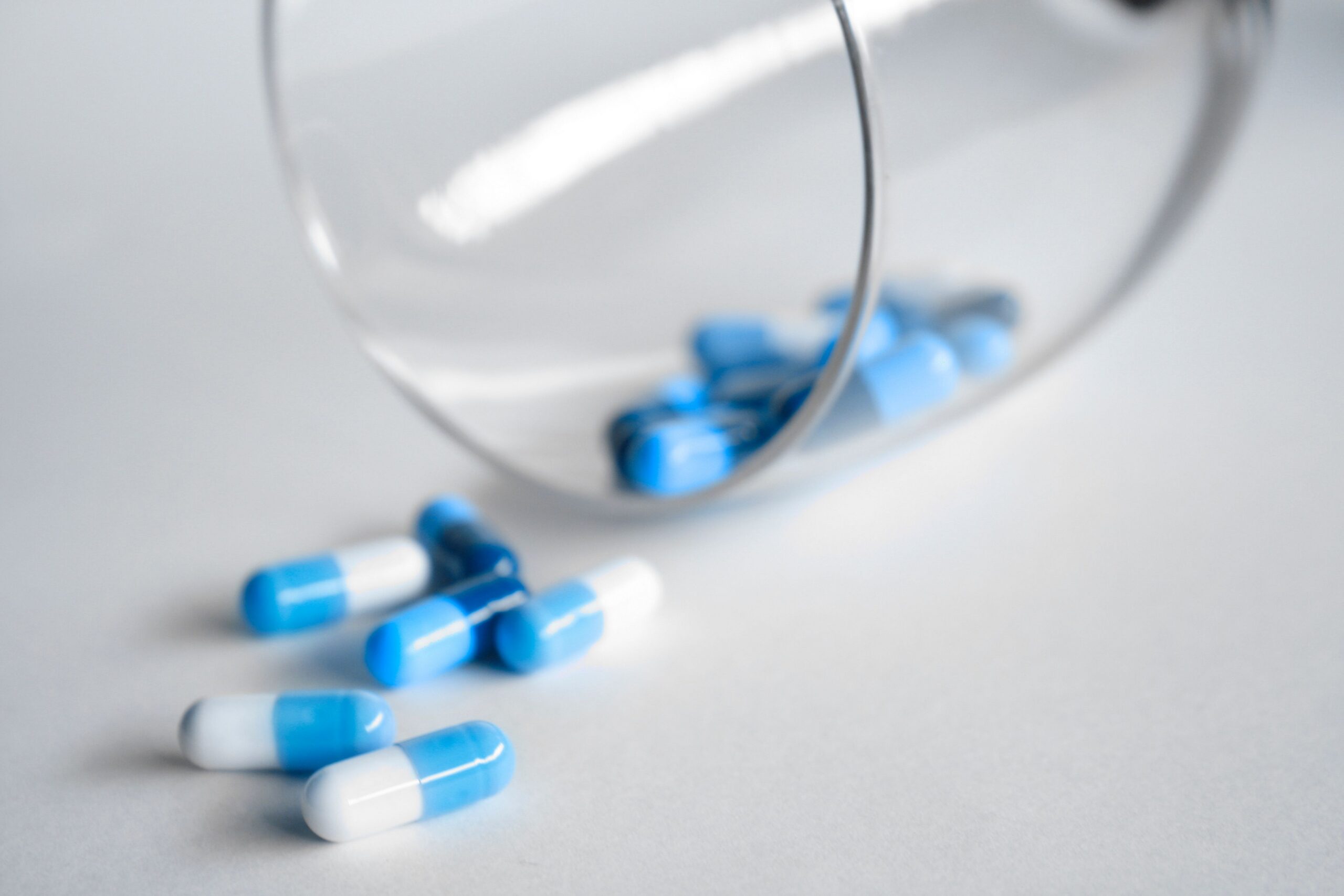 Blue-and-white capsules spilled from a glass container, representing an experimental oral medication being studied for pancreatic cancer treatment.