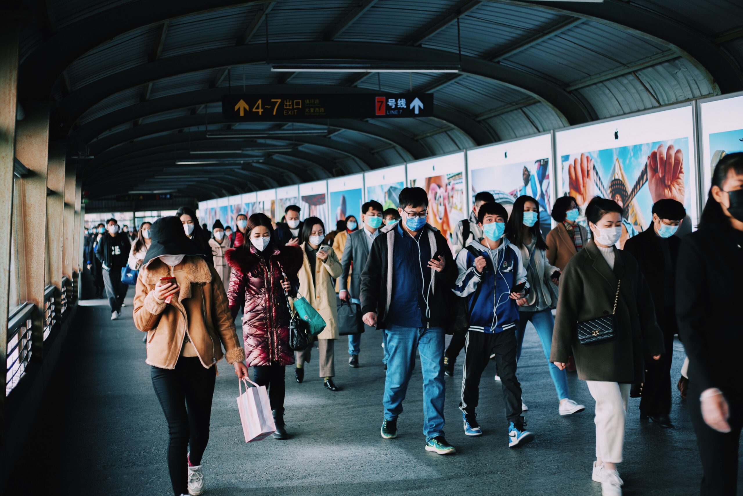 People wearing face masks walk through a crowded transit corridor, illustrating how infectious diseases can spread in densely populated public spaces during outbreaks and pandemics.
