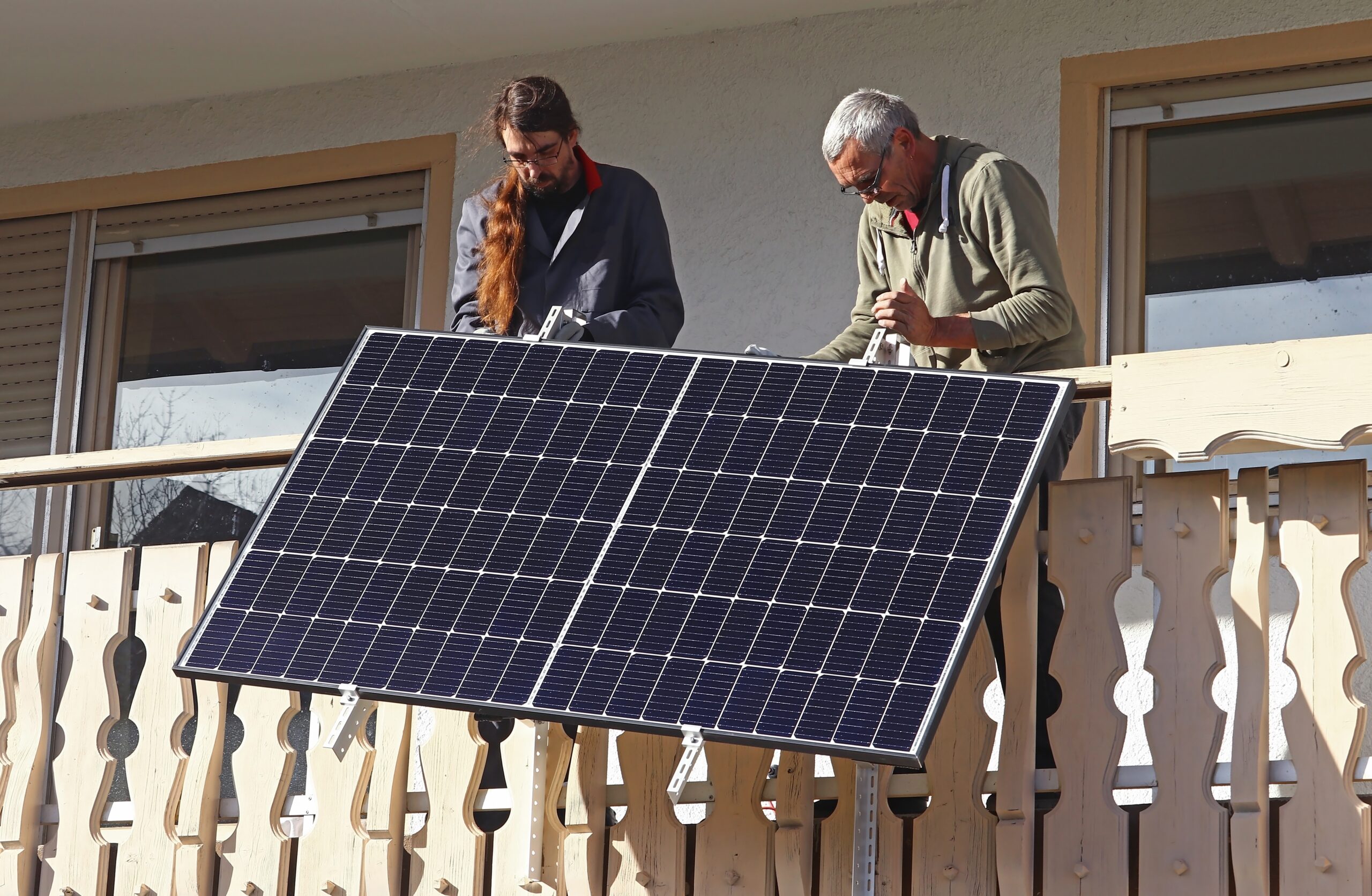 Two people installing a solar panel system on a residential balcony.