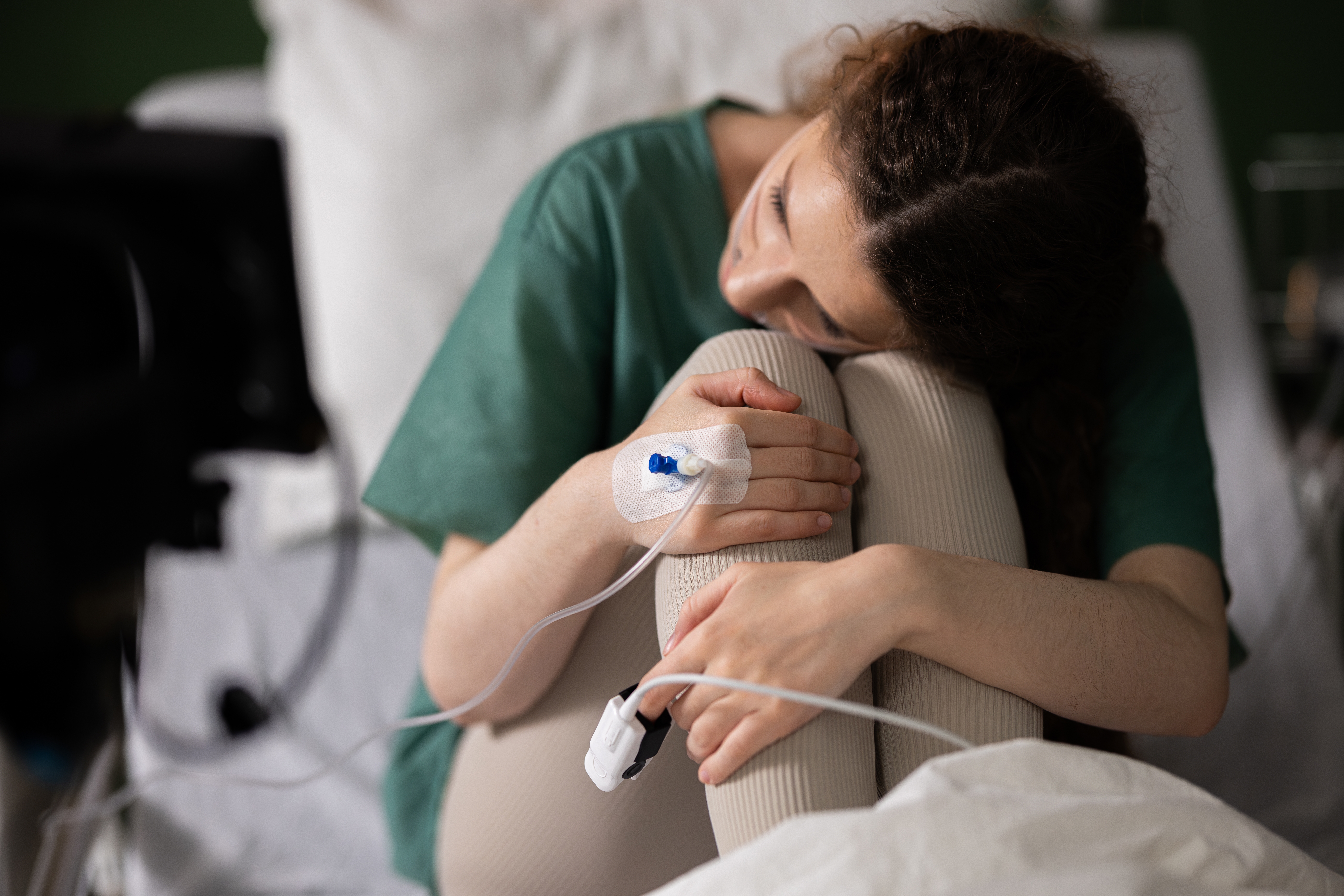 Hospital patient with an IV line sitting on a bed and embracing their knees.