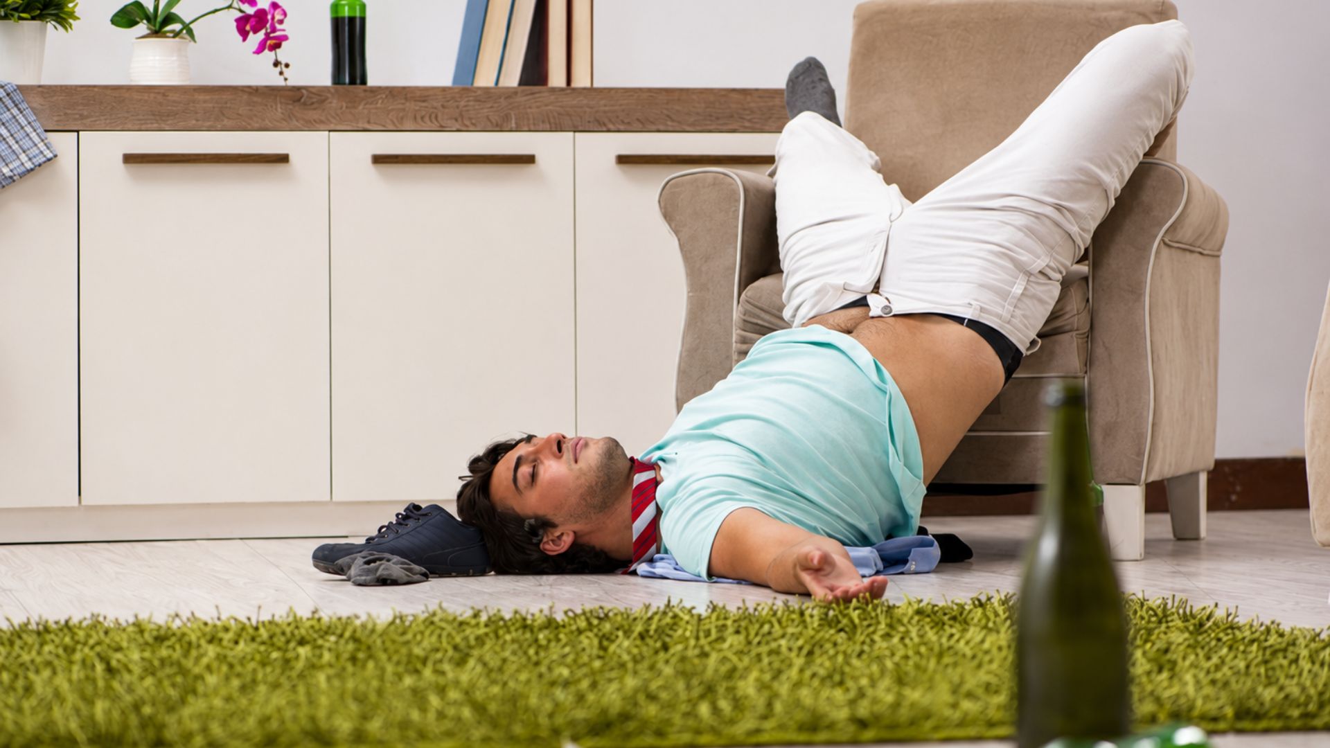 Man lying on the floor with his legs resting on a chair after drinking alcohol at home.
