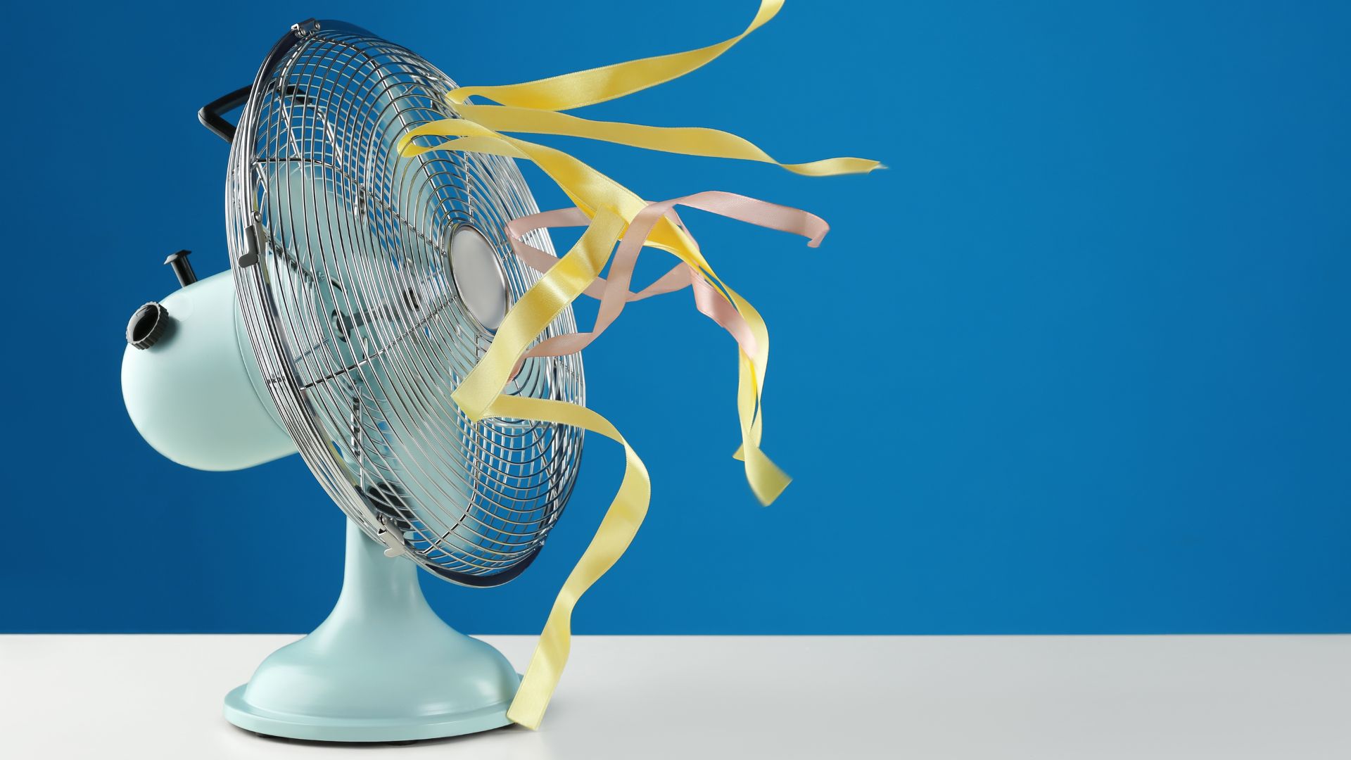 Retro tabletop fan blowing yellow and pink ribbons against a blue background.
