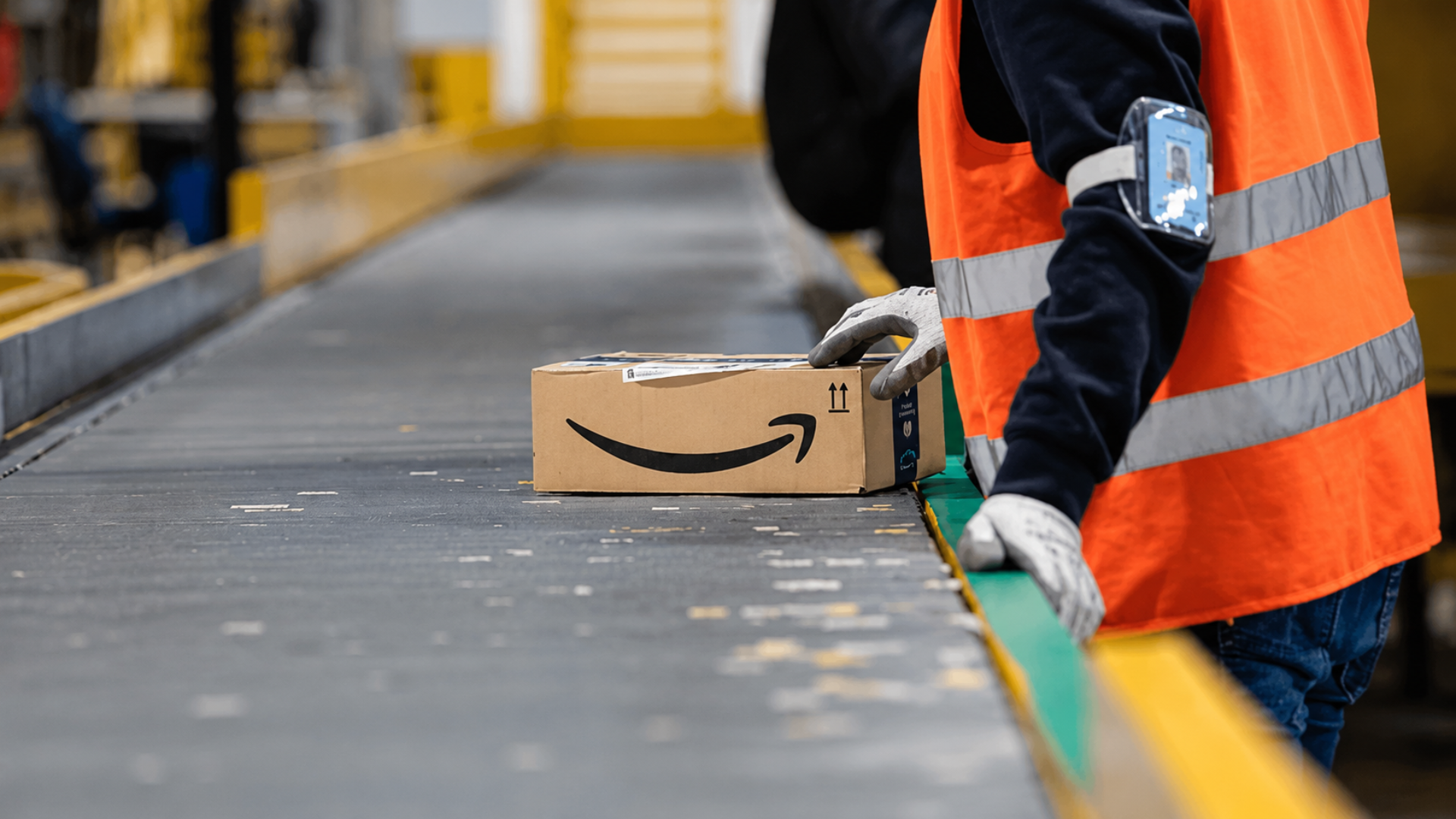 An Amazon warehouse worker guiding a cardboard box along a conveyor belt system.