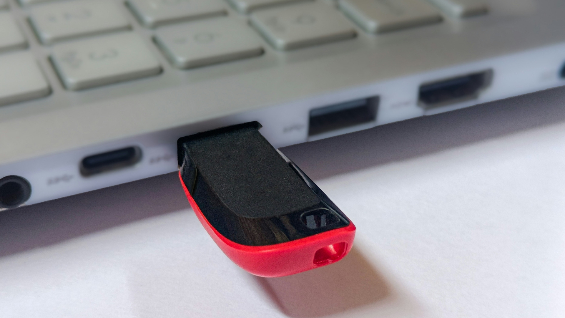 A red and black USB flash drive plugged into the USB port of a laptop.