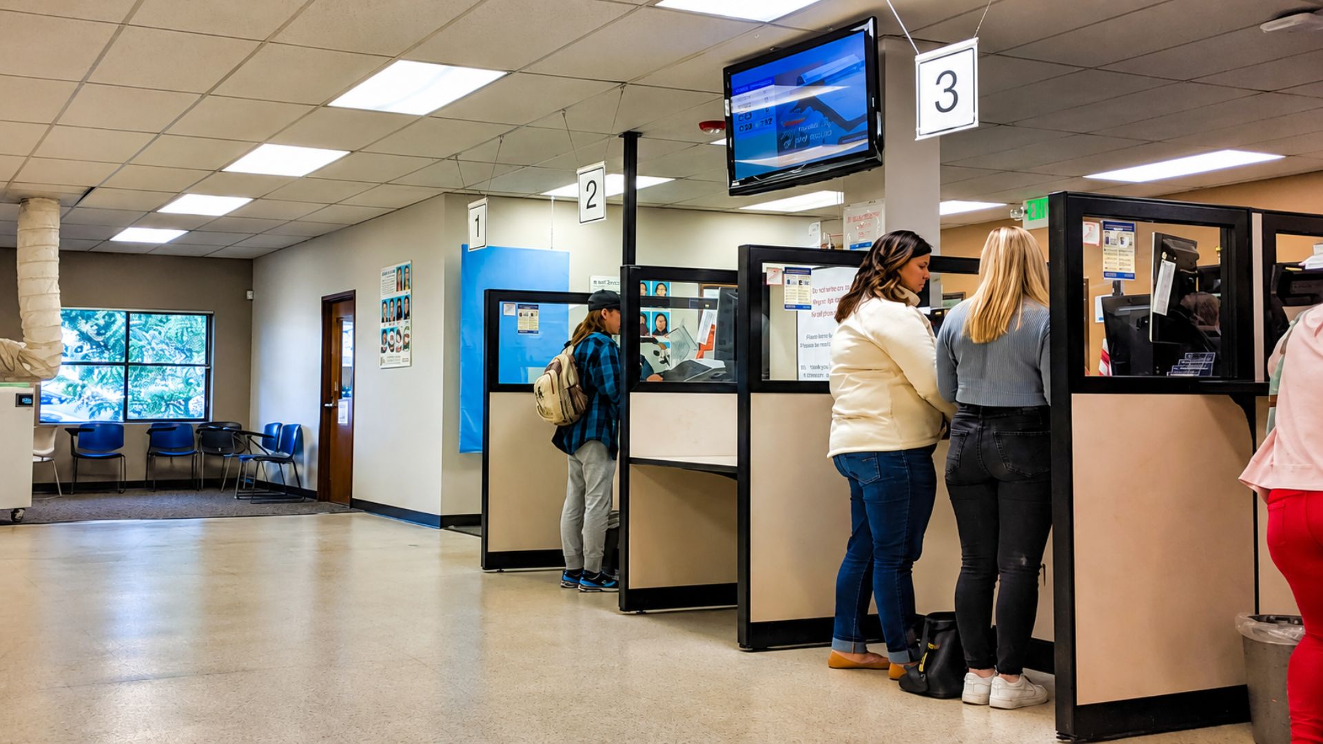 People wait at service counters inside a Department of Motor Vehicles office.