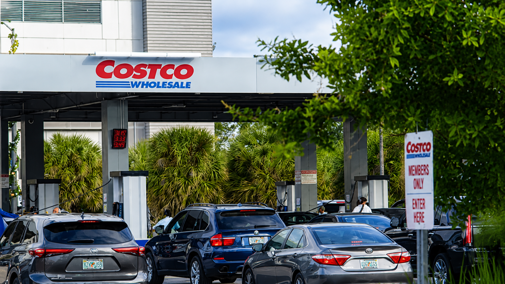A line of cars waiting to fuel at a busy Costco Wholesale gas station with an entrance sign visible.