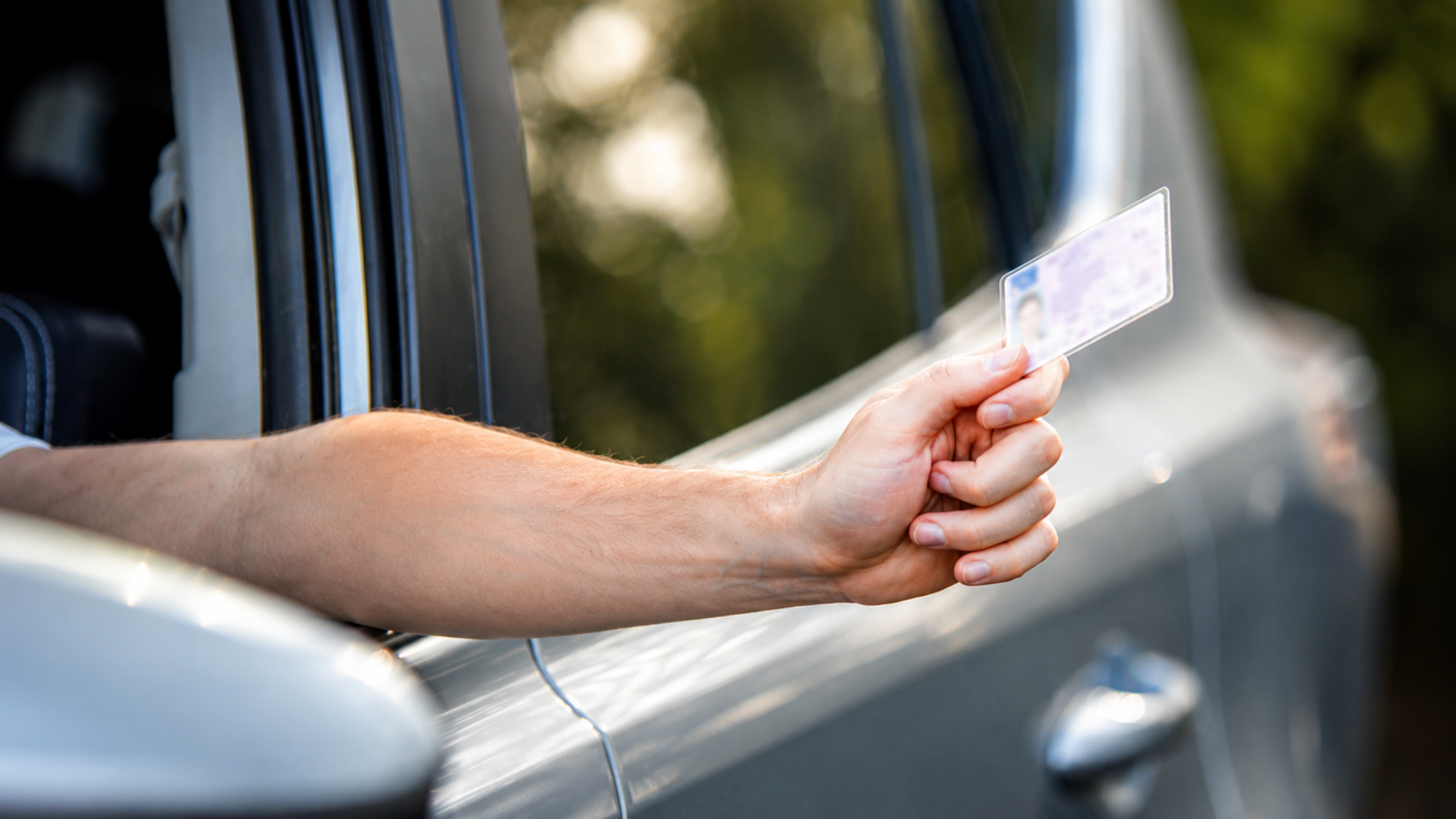 A person extending their arm out of a car window holding a driver's license card.