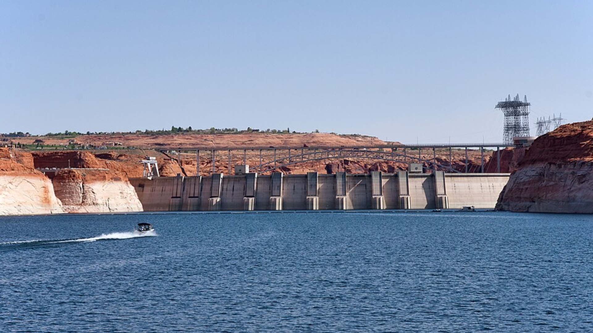 A boat traveling across Lake Powell in front of Glen Canyon Dam surrounded by exposed sandstone cliffs.