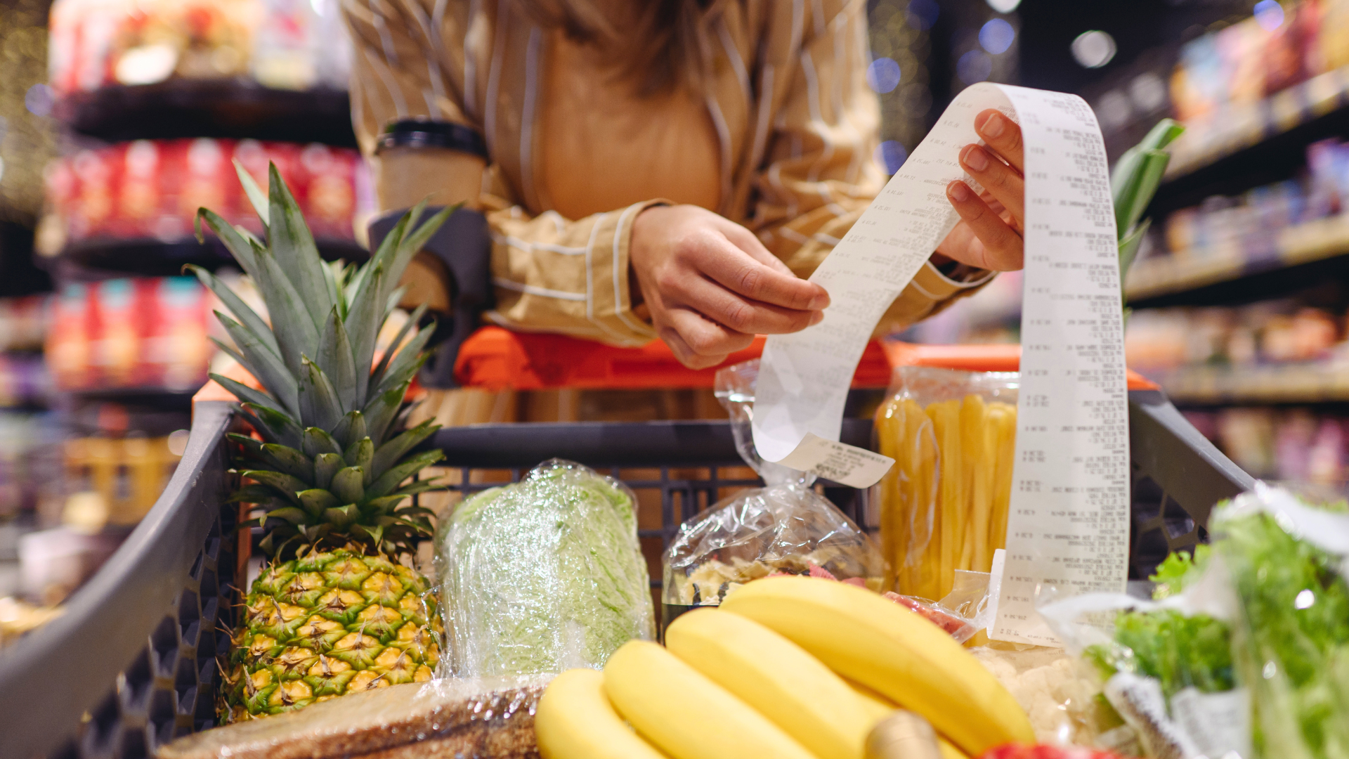 HERE ARE YOUR NEW SHORT AND SIMPLE ALT TEXTS! 🧾 Image 31: A close-up of a person holding a long receipt over a shopping cart full of fresh fruit and vegetables in a supermarket.