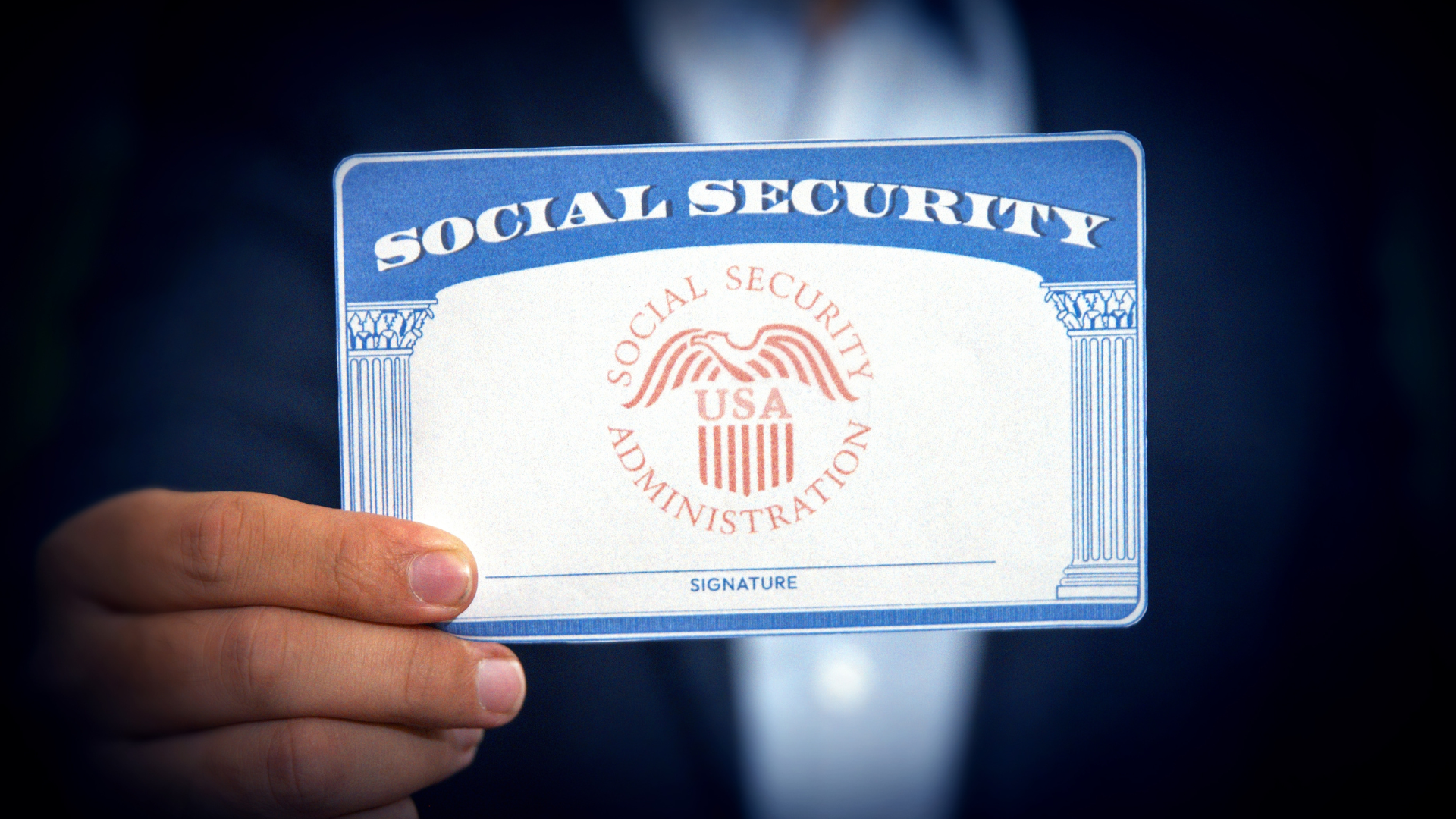 A close-up of a person's hand holding up a blue and white Social Security card.