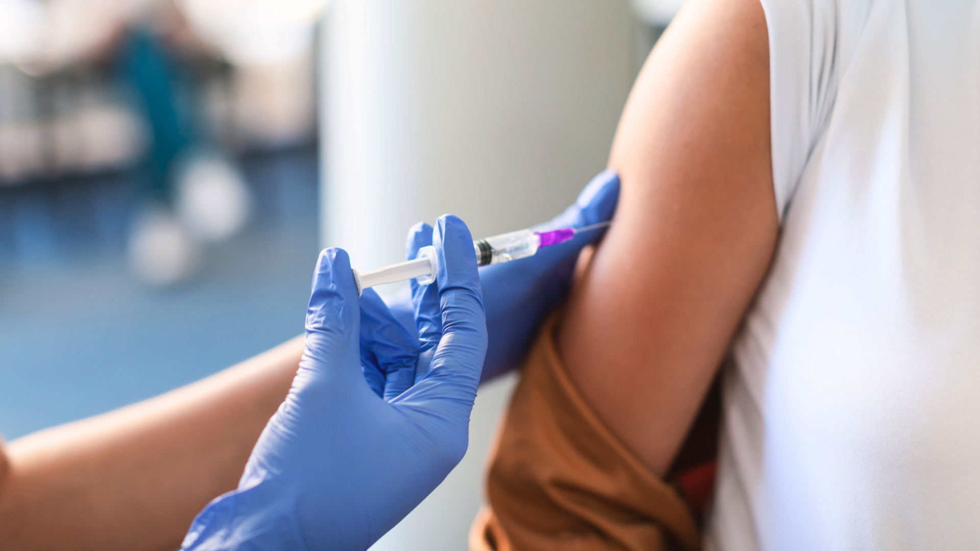 A close-up of a healthcare worker wearing blue gloves giving a vaccine injection into a patient's arm.