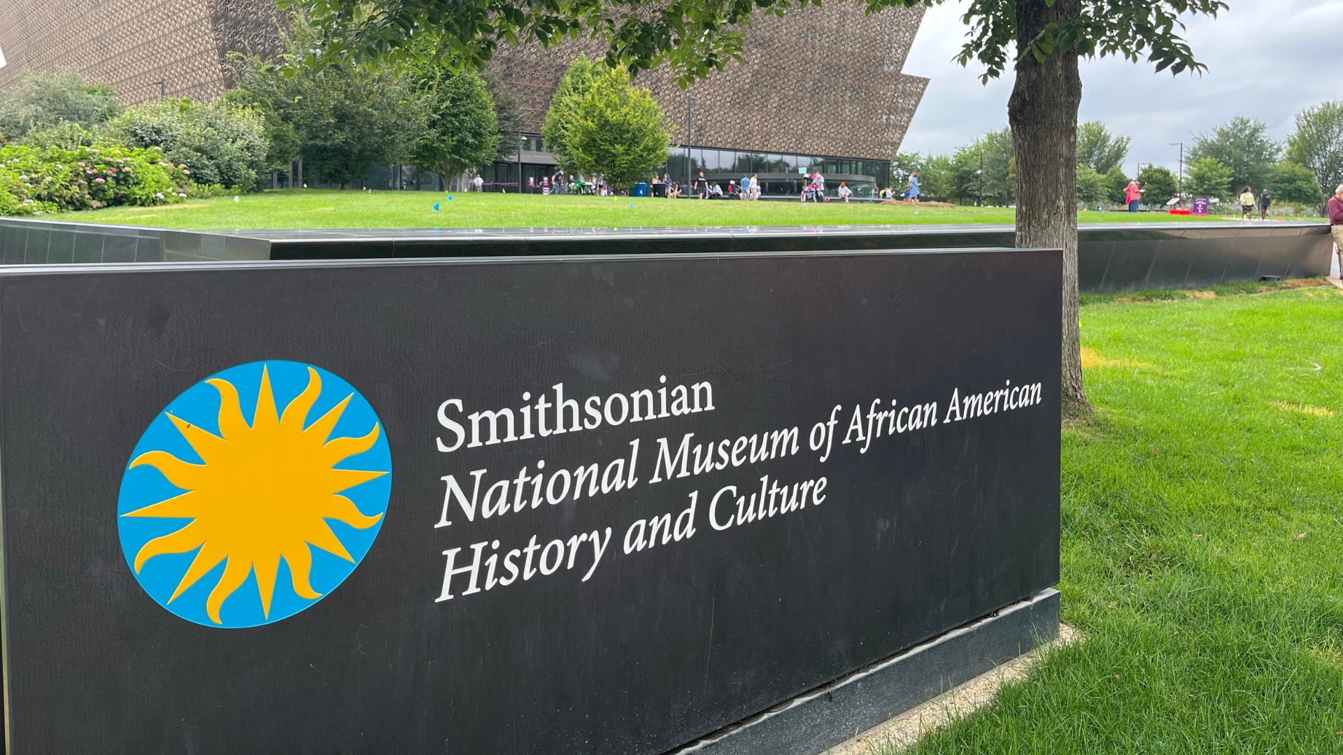 A large black sign displaying the logo and name of the "Smithsonian National Museum of African American History and Culture" standing on a grassy lawn.