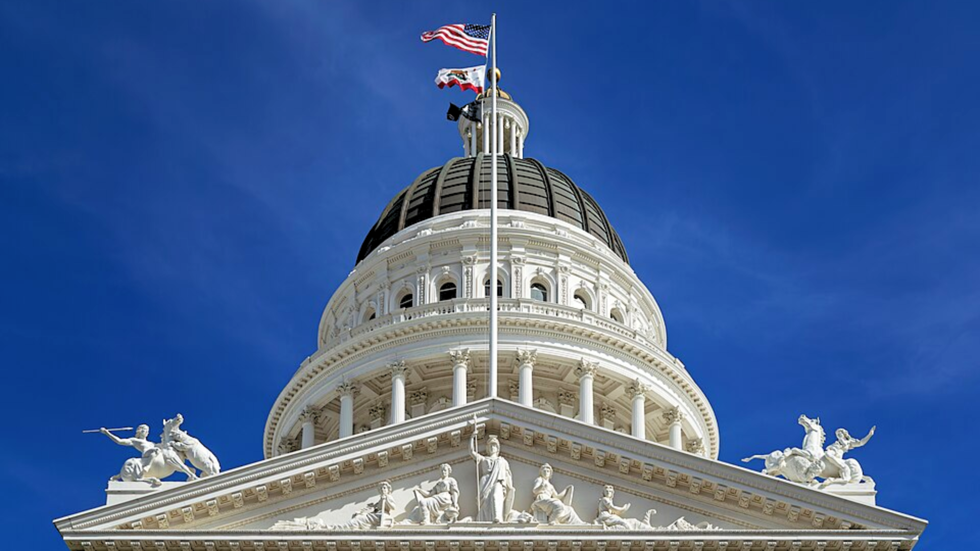 The white dome and ornate statues of the California State Capitol building under a clear blue sky.