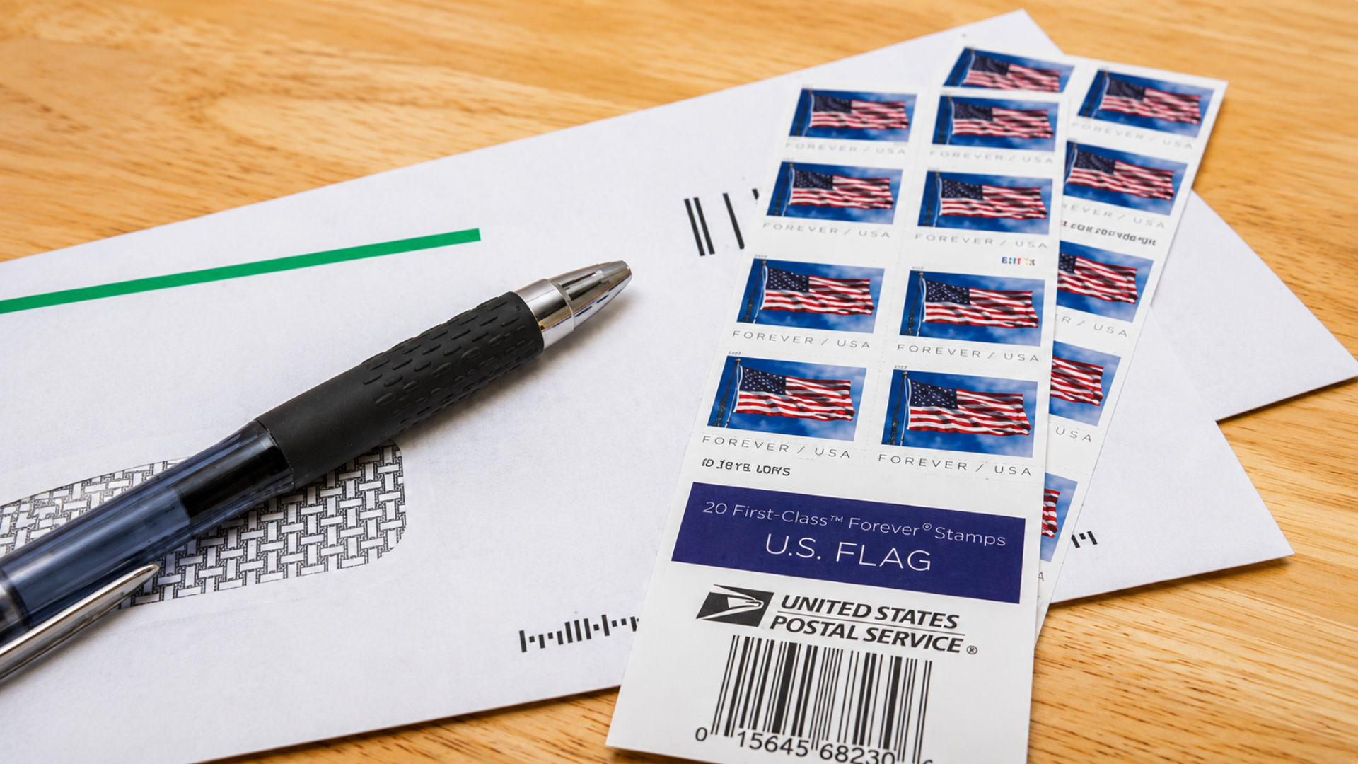 Sheet of USPS U.S. Flag Forever Stamps beside addressed envelopes and a pen on a wooden table.