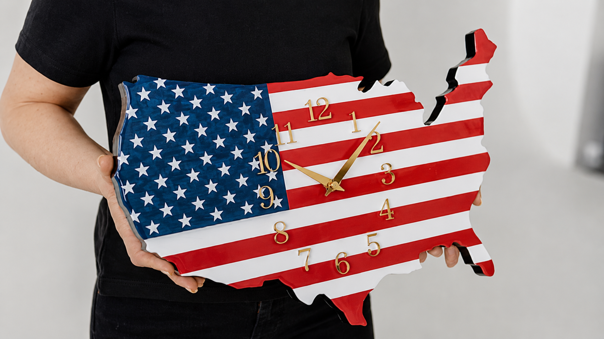 A person holding a wall clock shaped like the map of the United States and decorated with the American flag pattern.