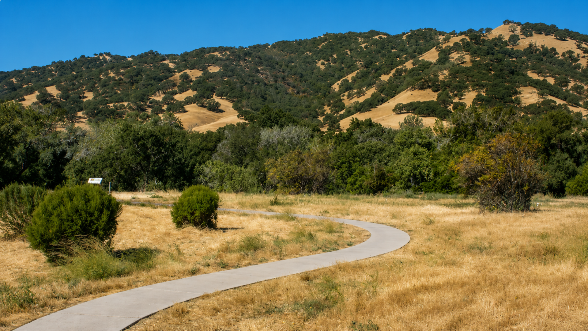 A paved walking path curving through open farmland and dry fields backed by rolling green hills in Solano County, California.