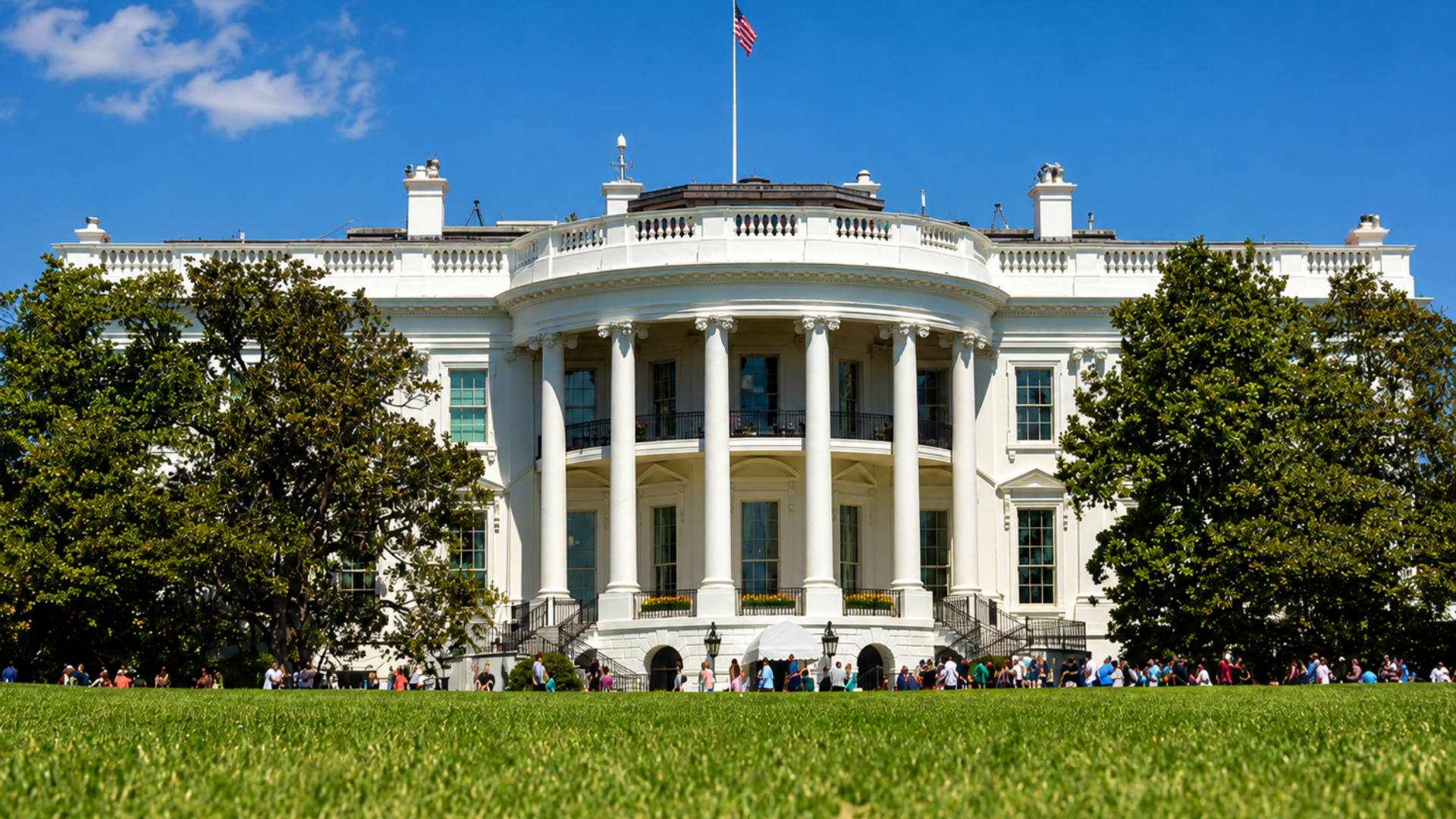 The South Portico of the White House with the American flag flying above and visitors on the South Lawn.
