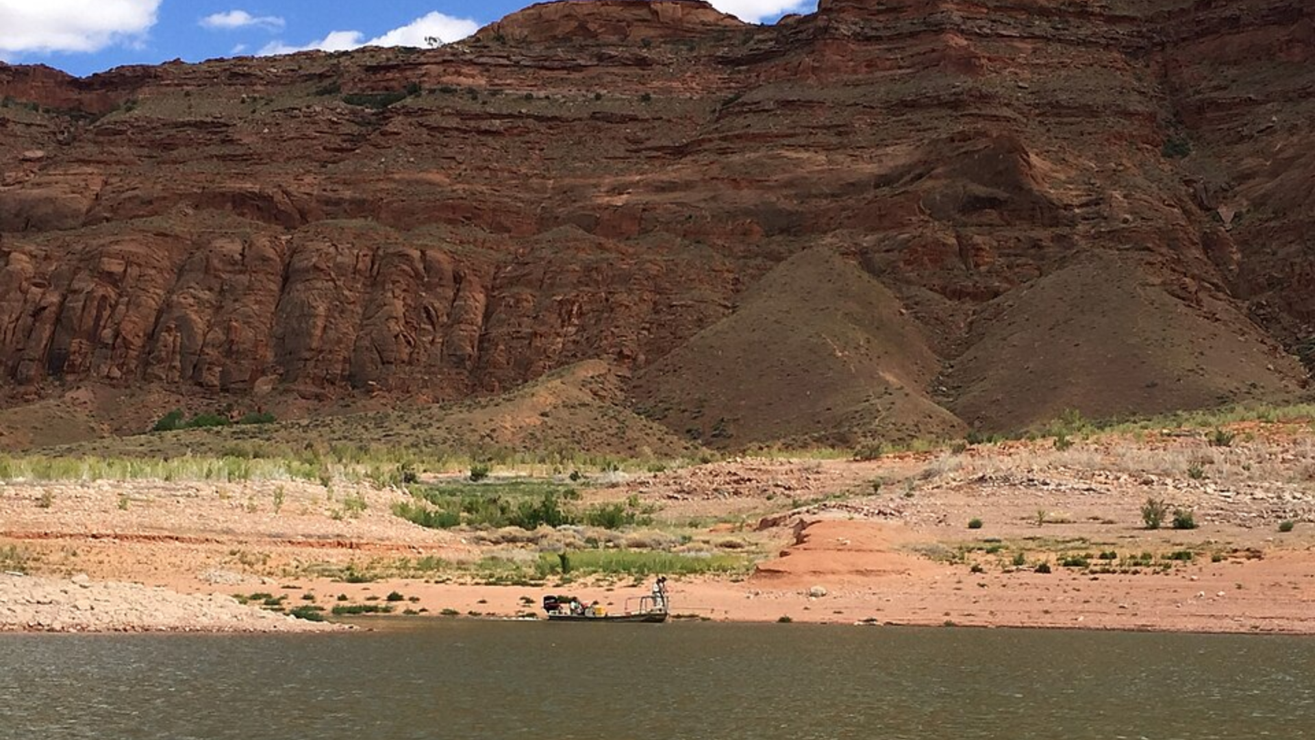 A small boat navigating the Colorado River along dry, steep canyon rock formations.