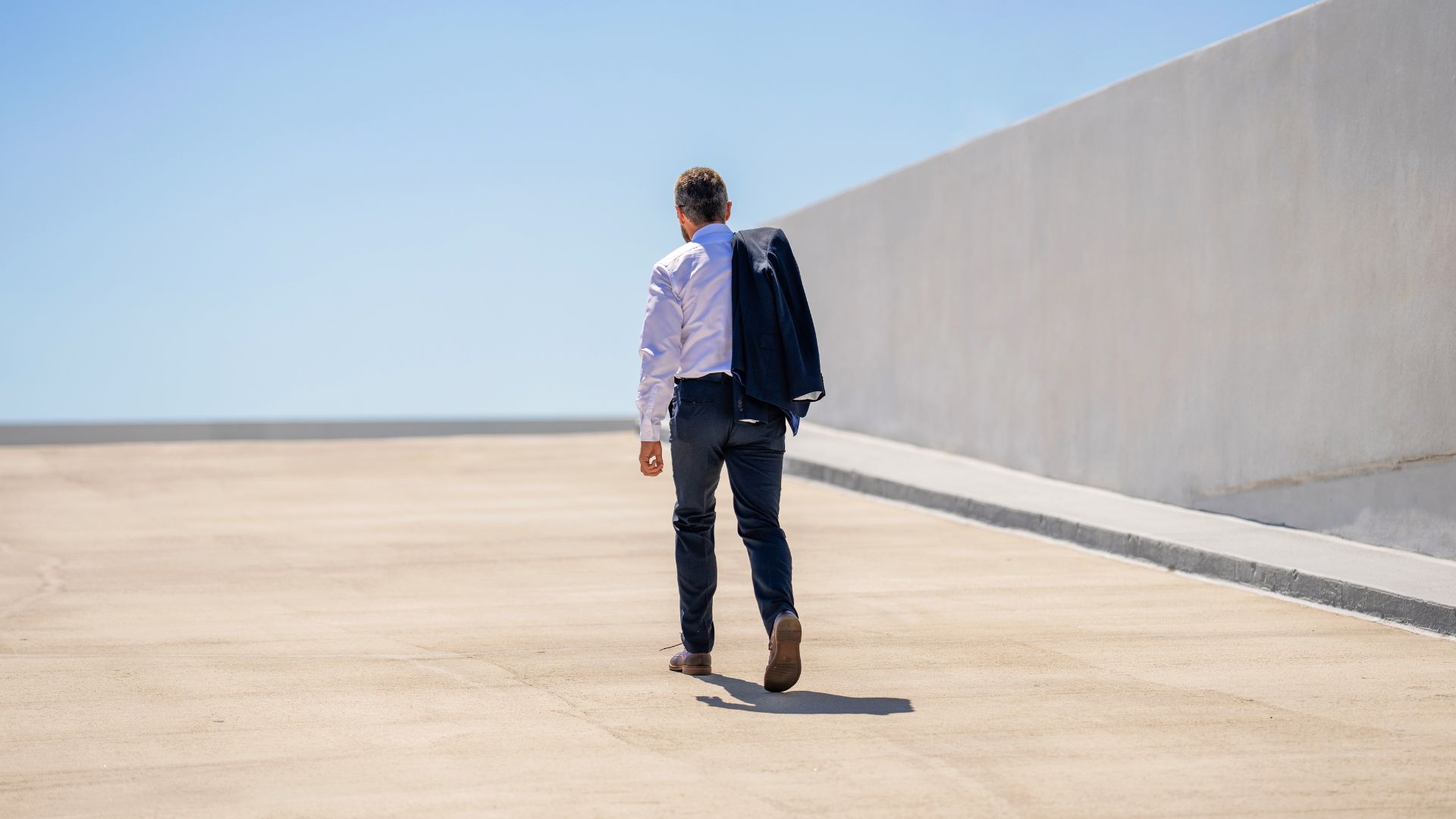 Worker walking away along an empty street with a wall on the right side.