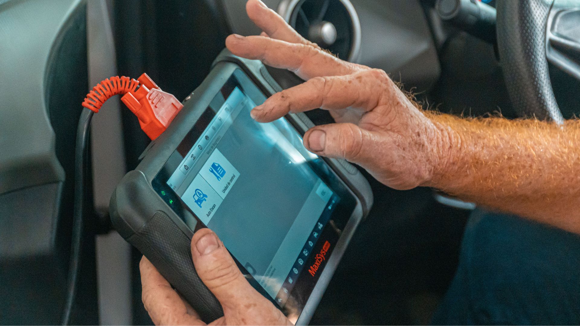 Technician holding diagnostic scan tool connected to car dashboard port.