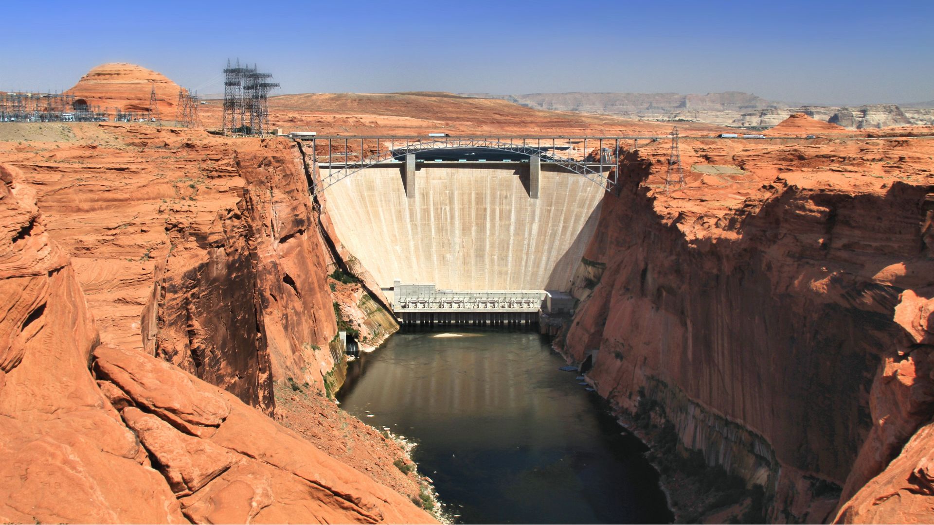 Glen Canyon Dam holding back the Colorado River, flanked by red sandstone cliffs.