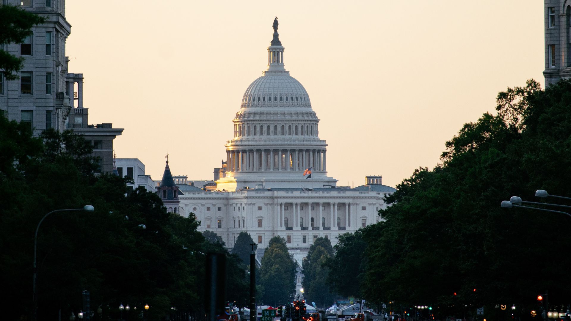 Wide shot of the U.S. Capitol building at dusk, framed by trees.