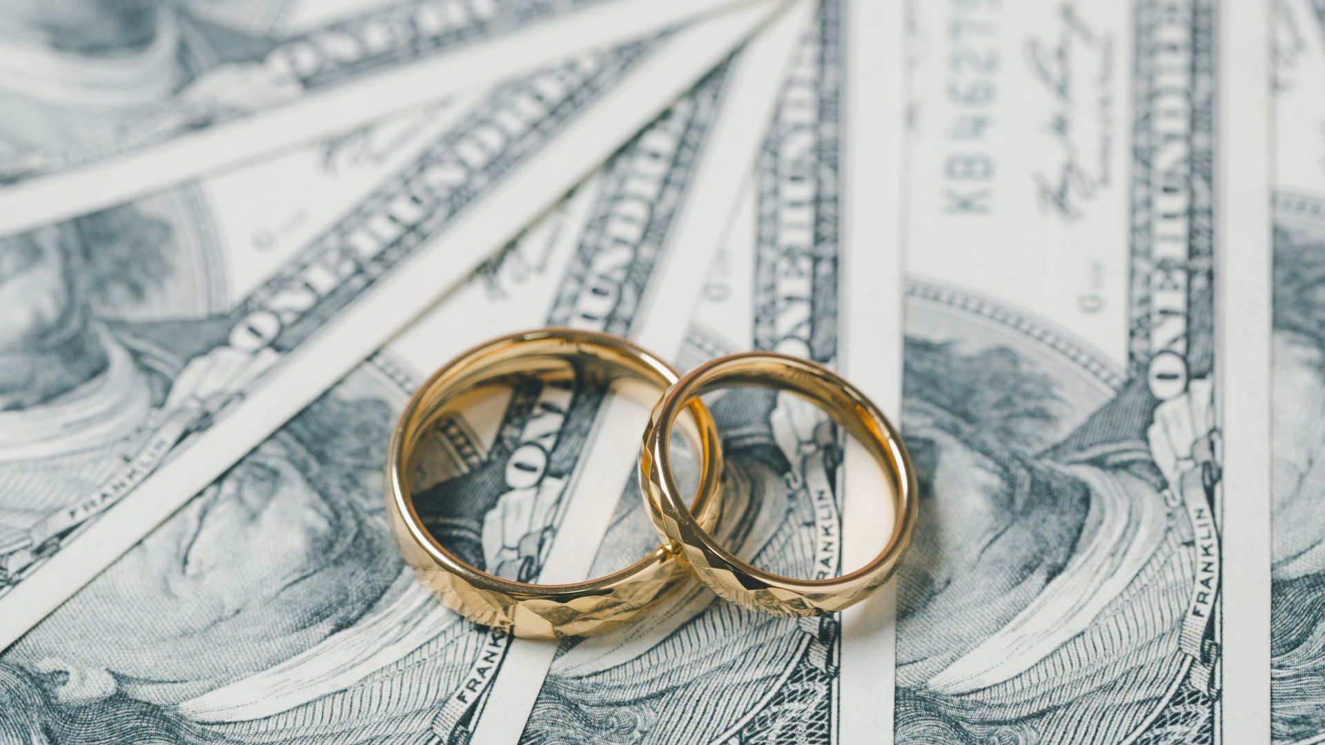 Two gold wedding rings resting on hundred dollar bills.