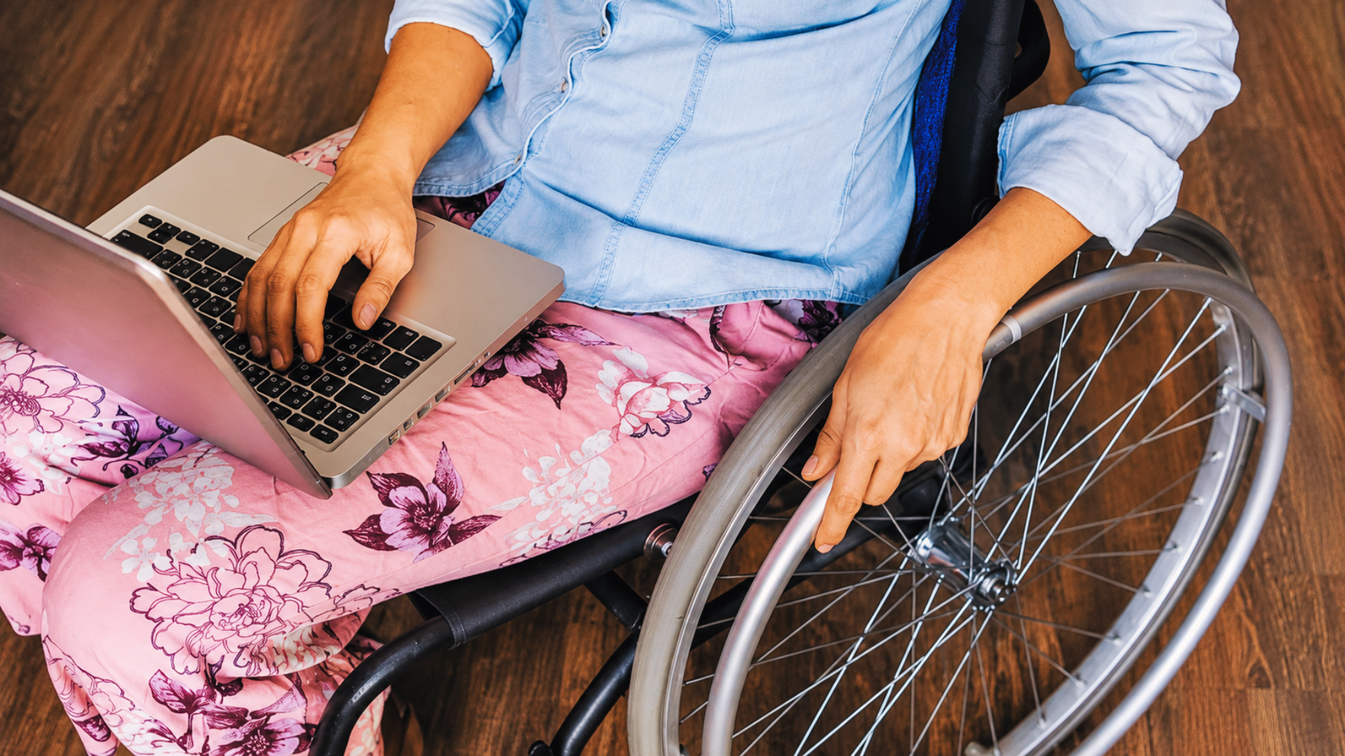 A person in a wheelchair working on a laptop computer resting on their lap.