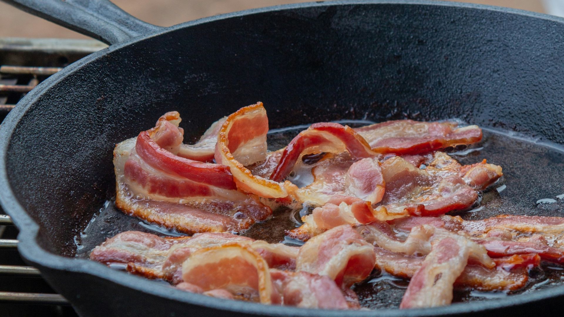 Strips of bacon sizzling in a cast-iron skillet.