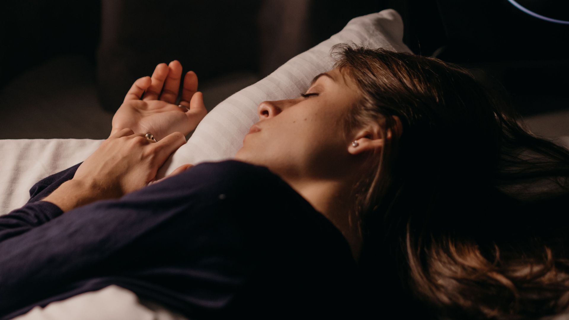 Woman lying in bed with her eyes closed in a darkened room.
