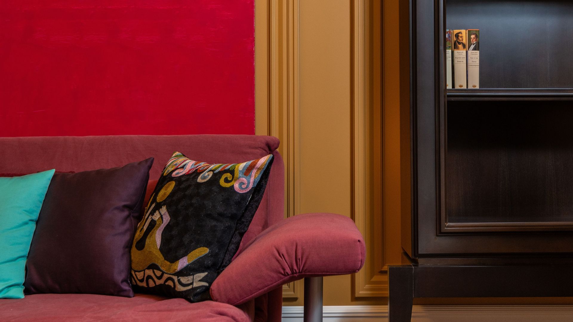 Pink sofa with colorful pillows beside dark shelving in a vibrant living room.