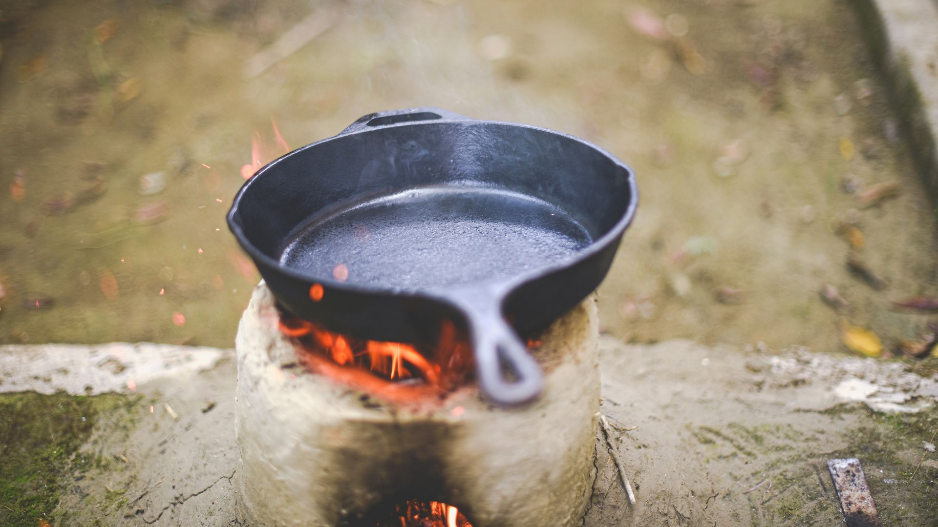 Cast-iron skillet heating over an outdoor open flame.