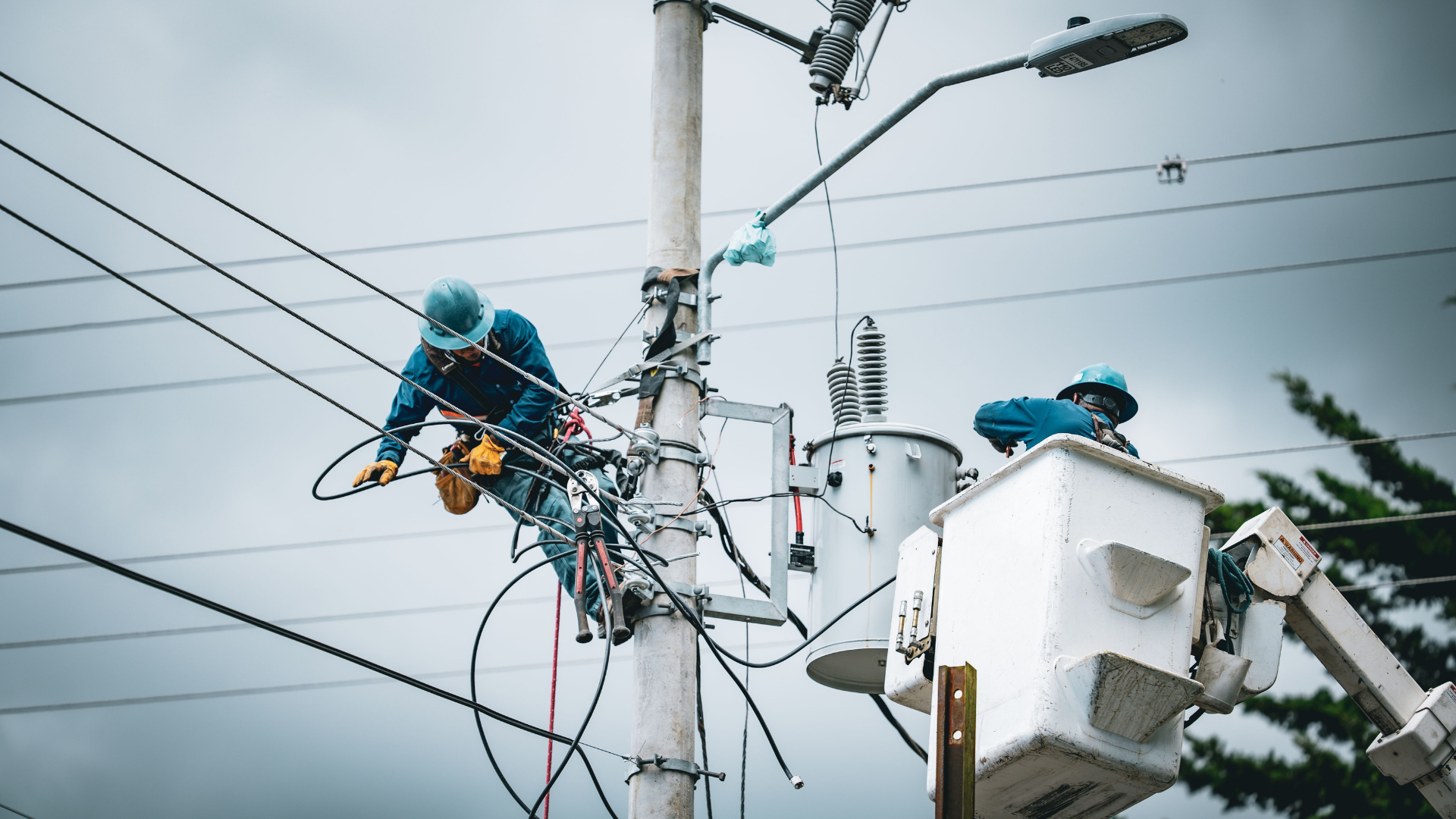 Electricians repairing power lines, illustrating the "traffic jam" of transmission congestion driving up electricity bills.