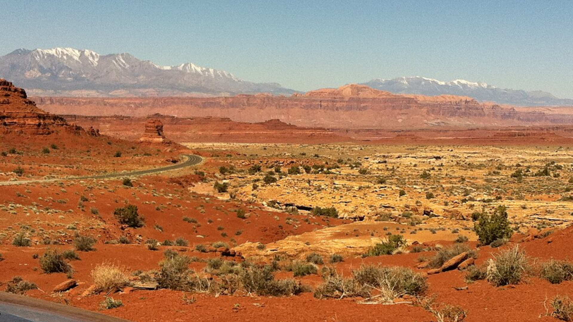 Red desert landscape with a winding road and snowcapped mountains in southeastern Utah.