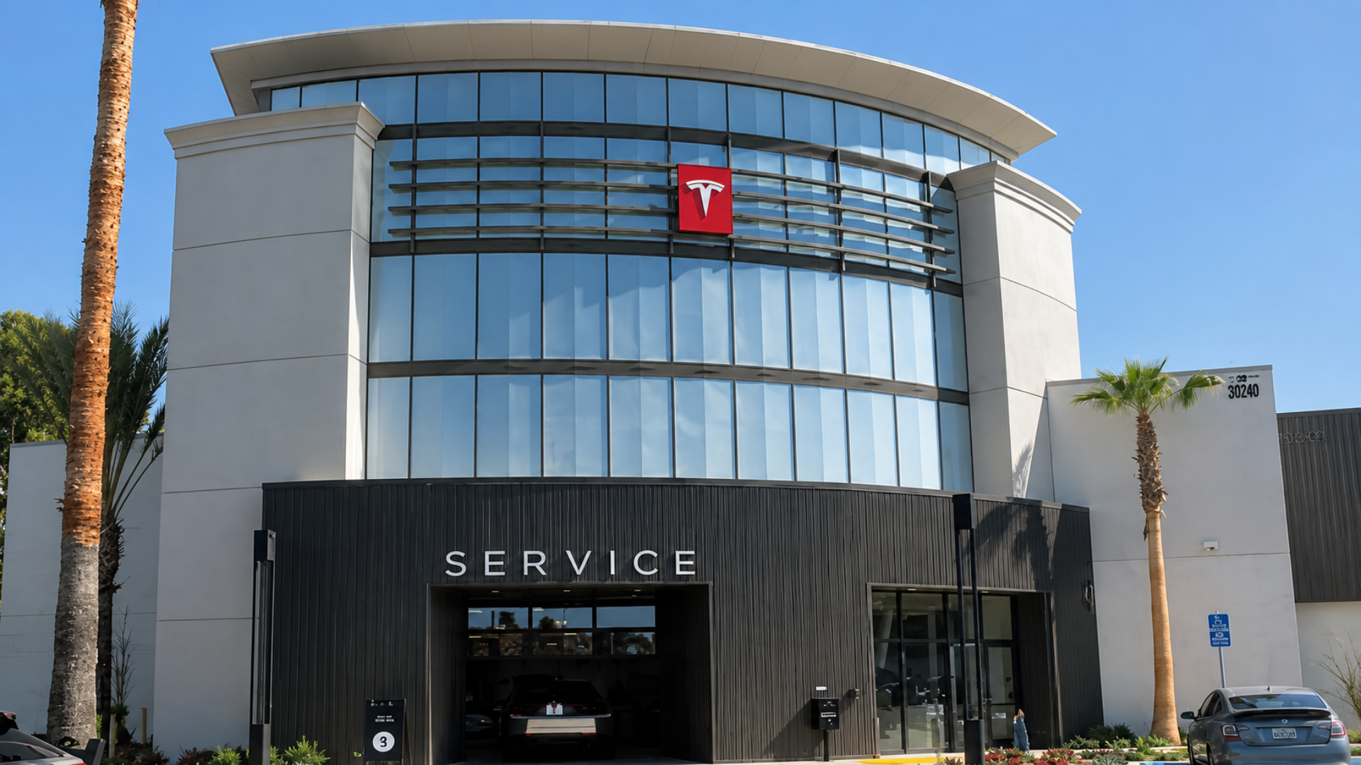 Modern Tesla Service Center building with large glass windows and palm trees.