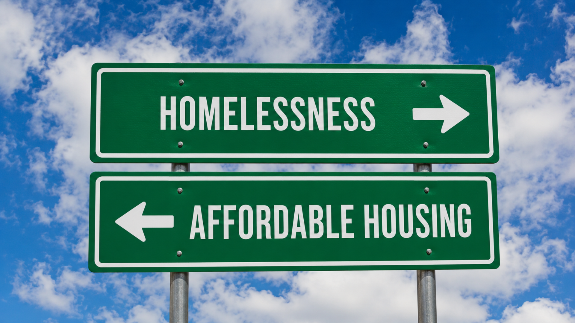 Green road sign with arrows pointing to "Homelessness" and "Affordable Housing."