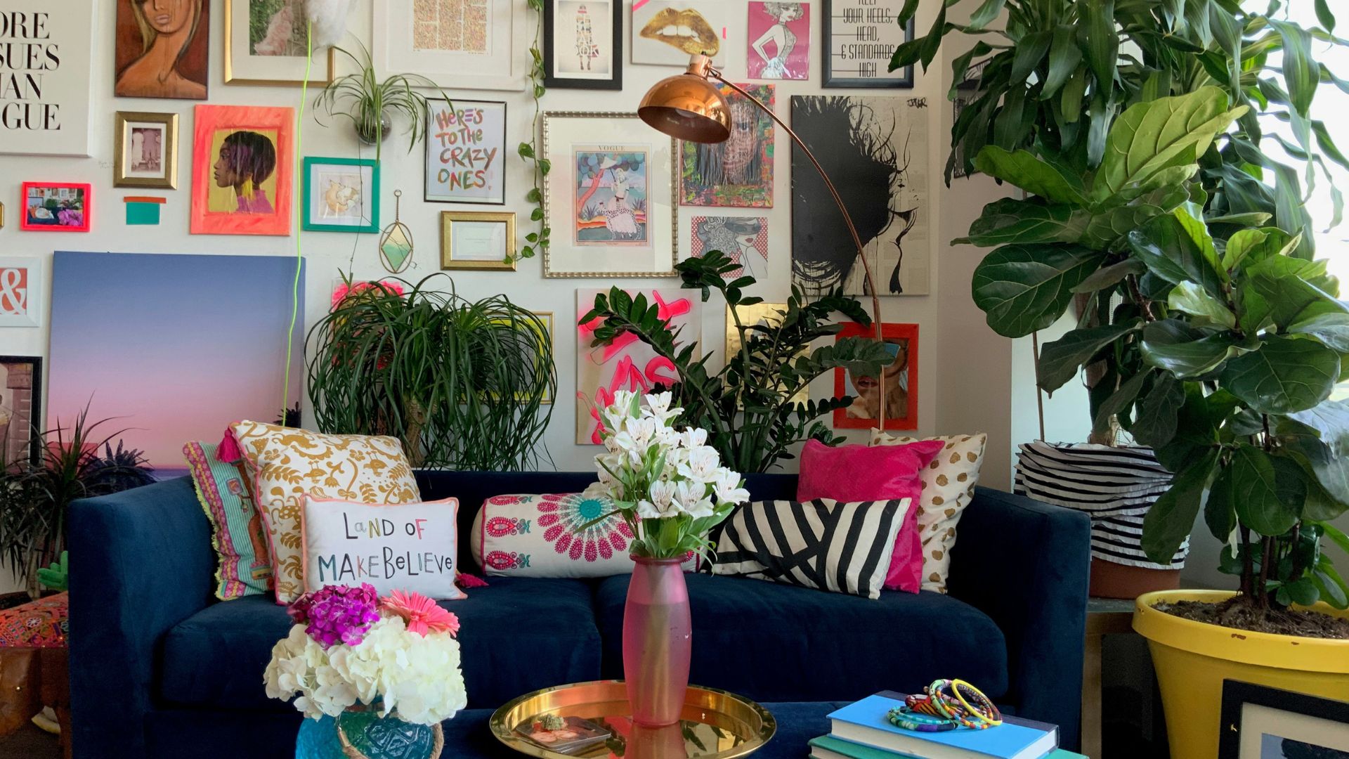 Colorful living room with blue sofa, patterned pillows, wall art, and large houseplants.