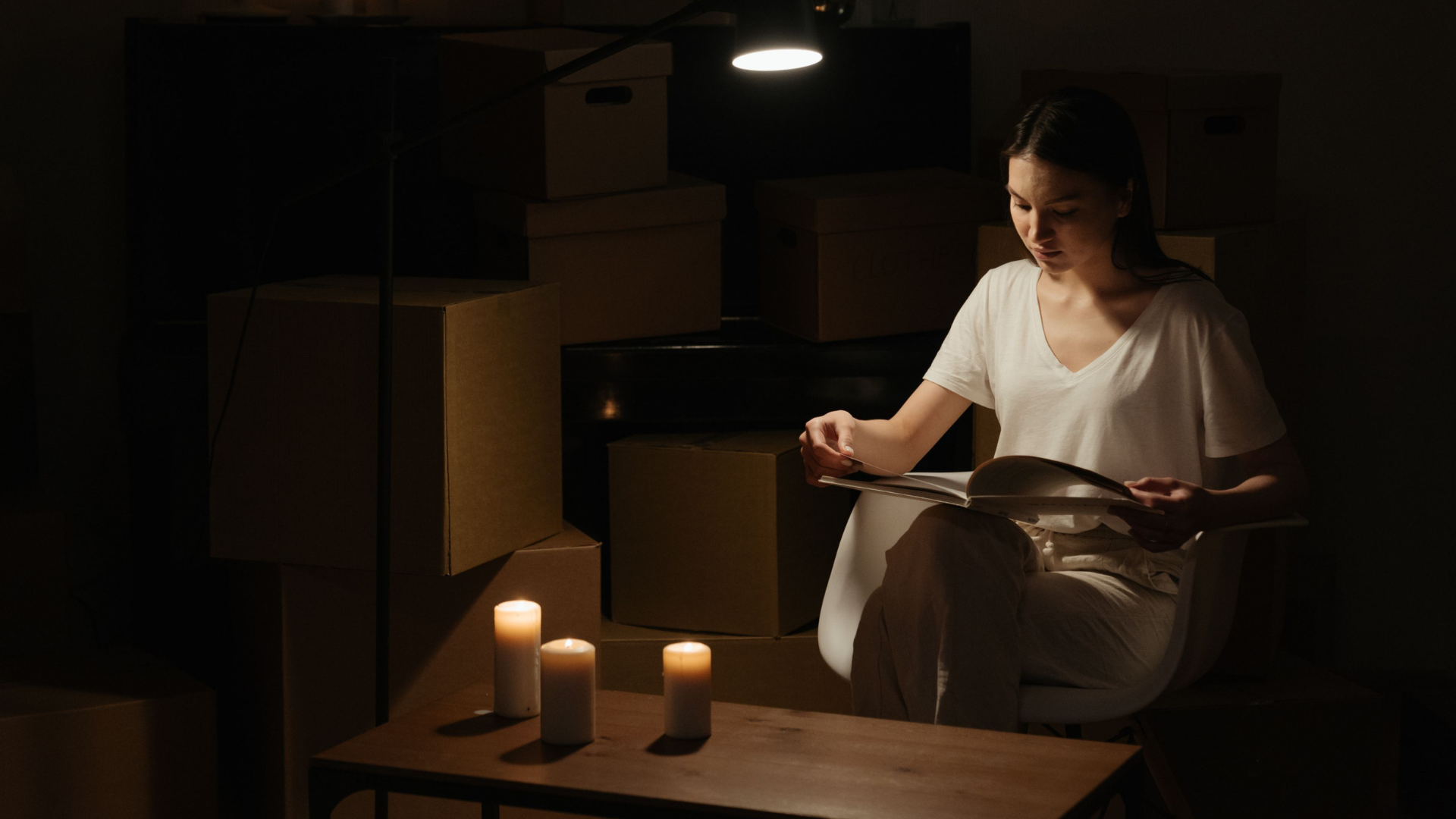 A woman reading in an apartment setting, surrounded by boxes and candlelight.