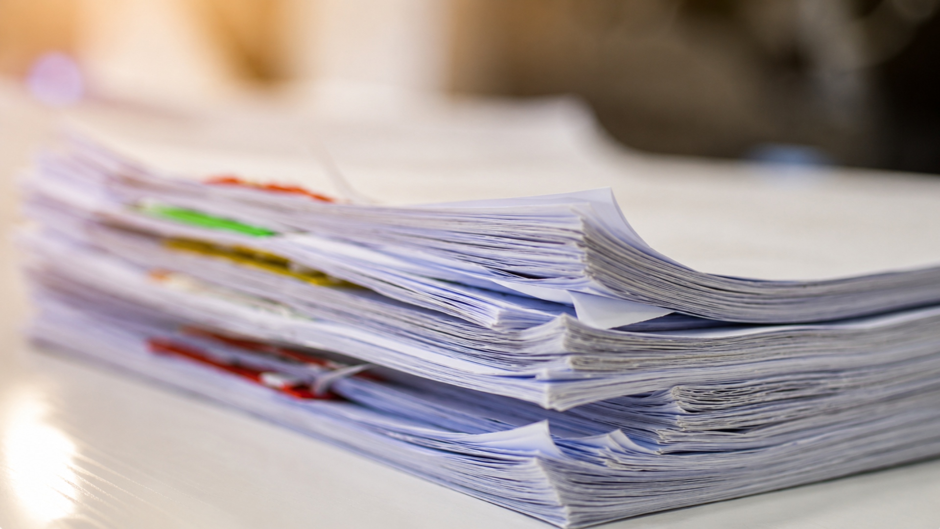 A thick stack of printed academic papers and research documents with colorful sticky tabs resting on a desk.