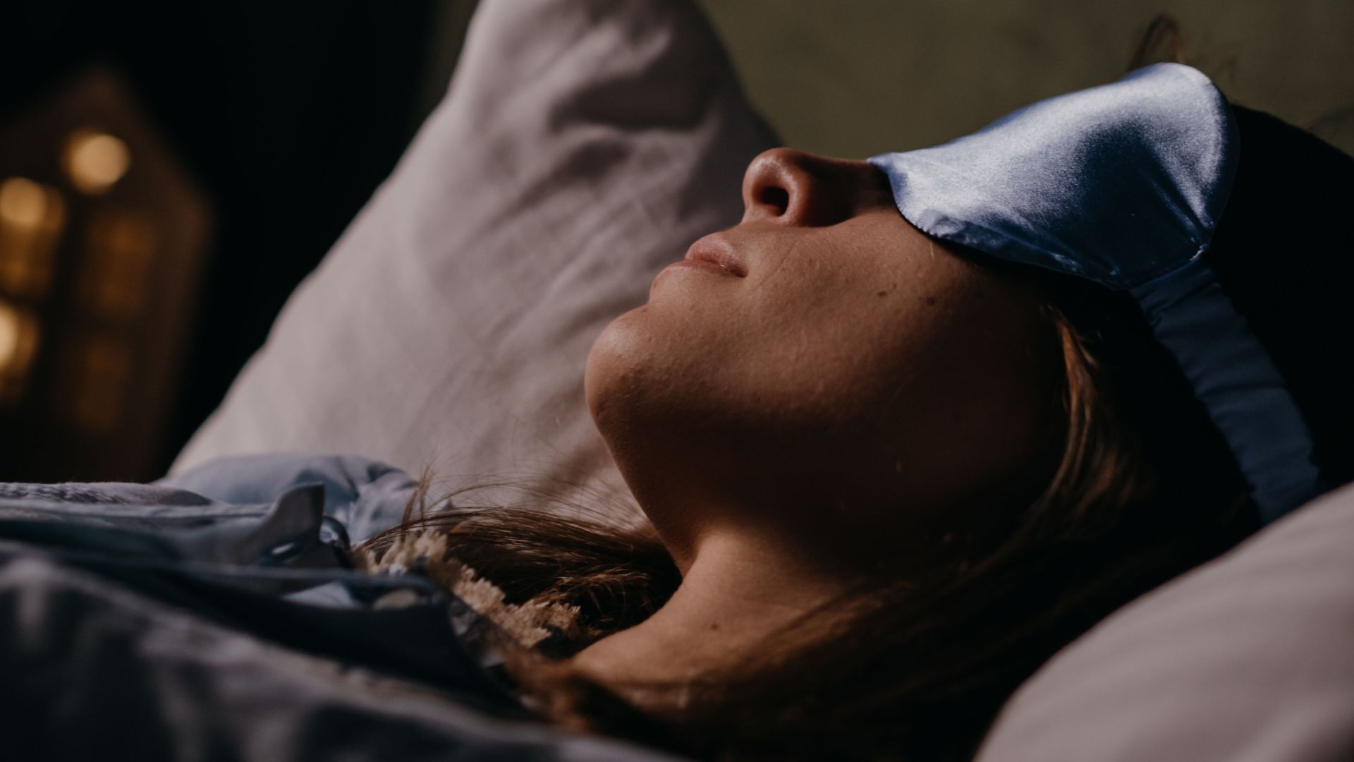Woman sleeping in bed while wearing a blue eye mask.