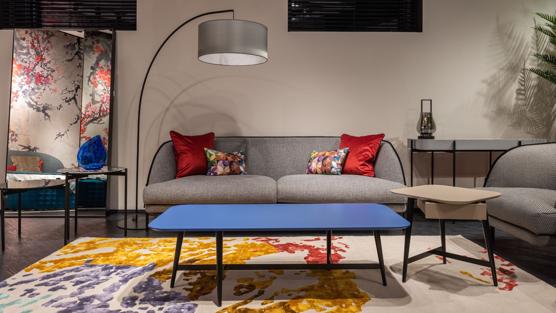 Modern living room with gray sofa, colorful rug, blue coffee table, and arched floor lamp.